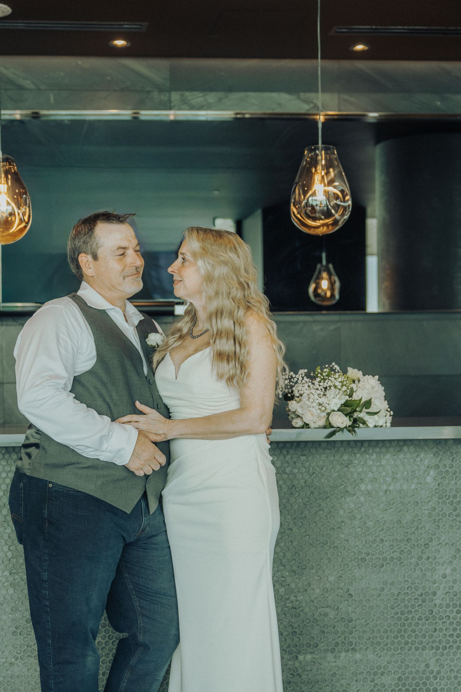 Bride and groom sharing a romantic moment in a modern venue with warm pendant lights on their wedding day.