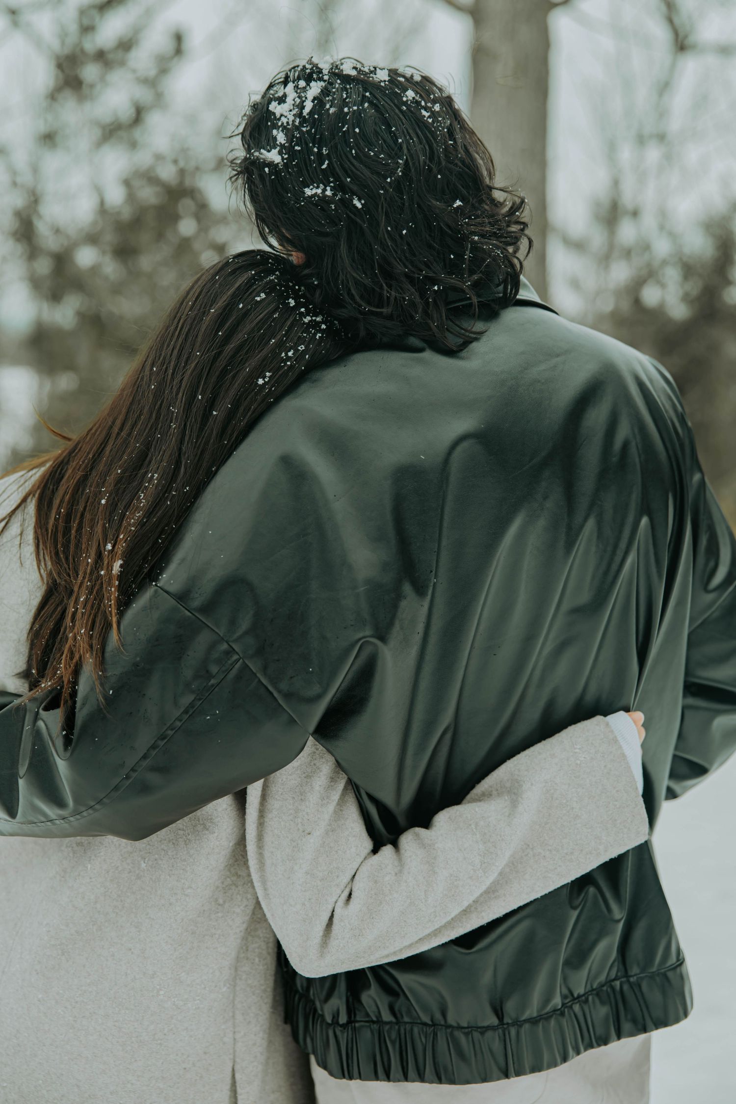 Back view of couple wearing matching black and gray windbreakers walking together in snowy winter setting.