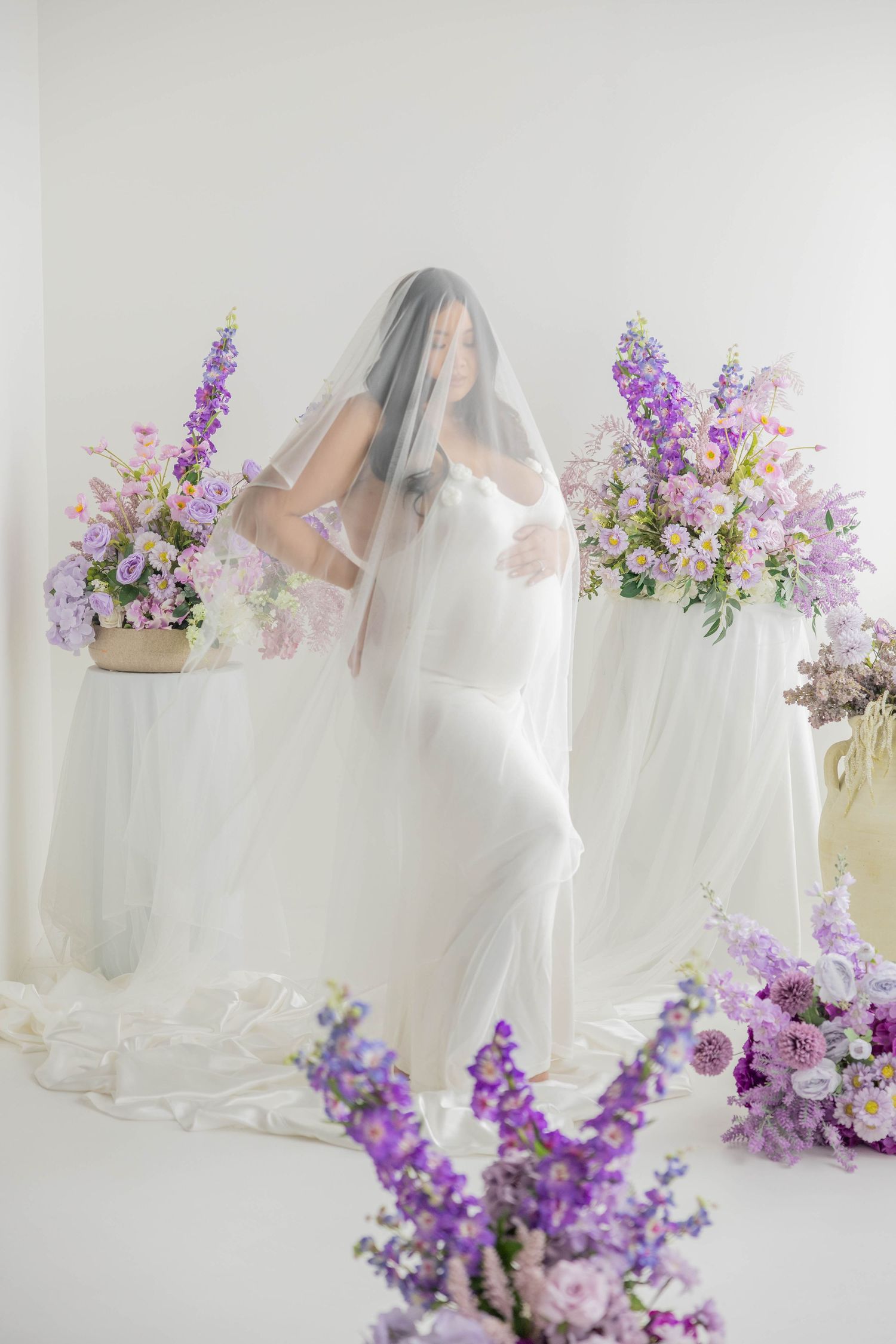 Ethereal bridal portraits with flowing white veil and delicate purple floral arrangements creating a romantic atmosphere.