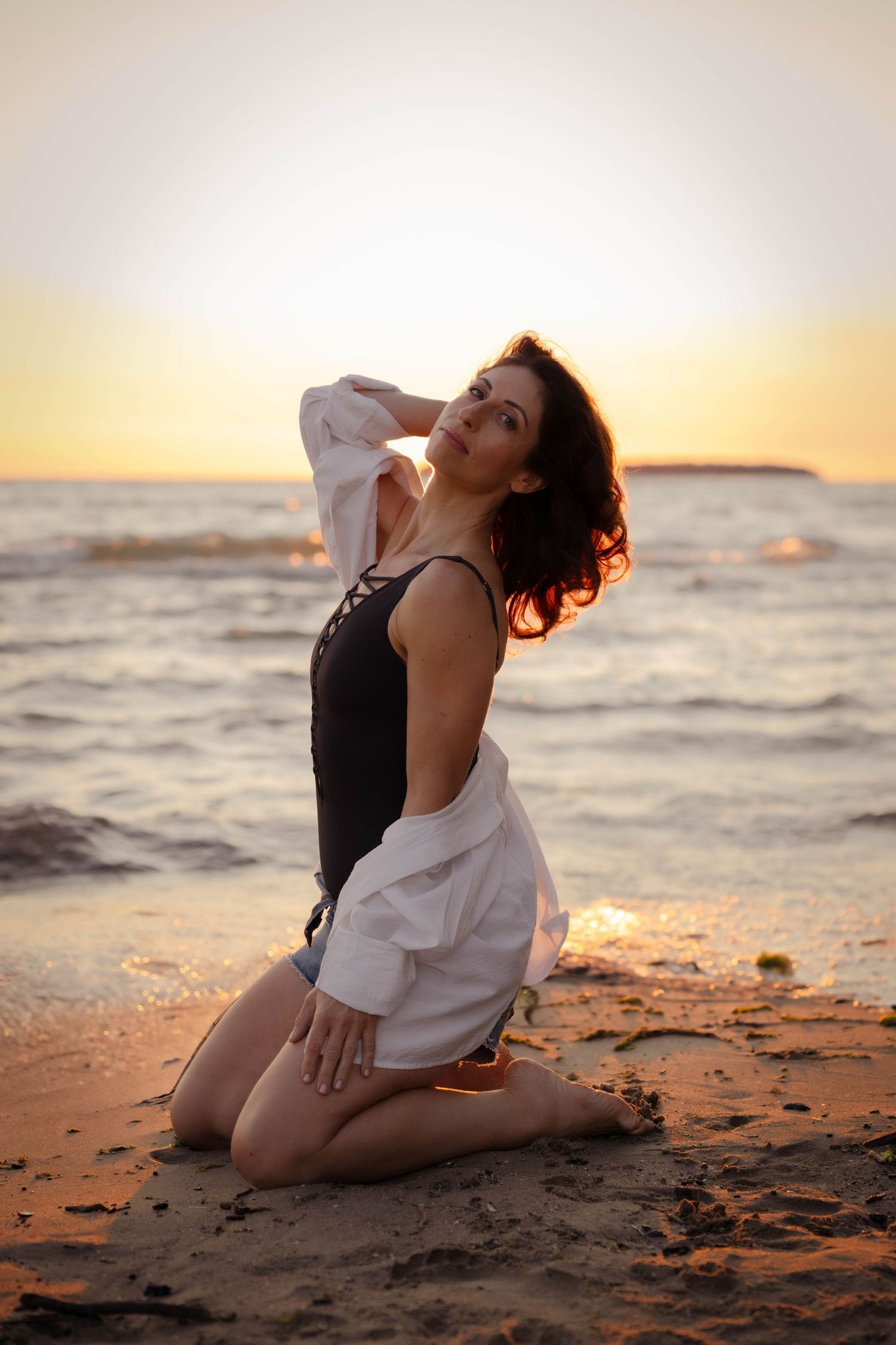 A person in a white top poses gracefully on a beach at sunset creating an artistic silhouette against the golden sky.