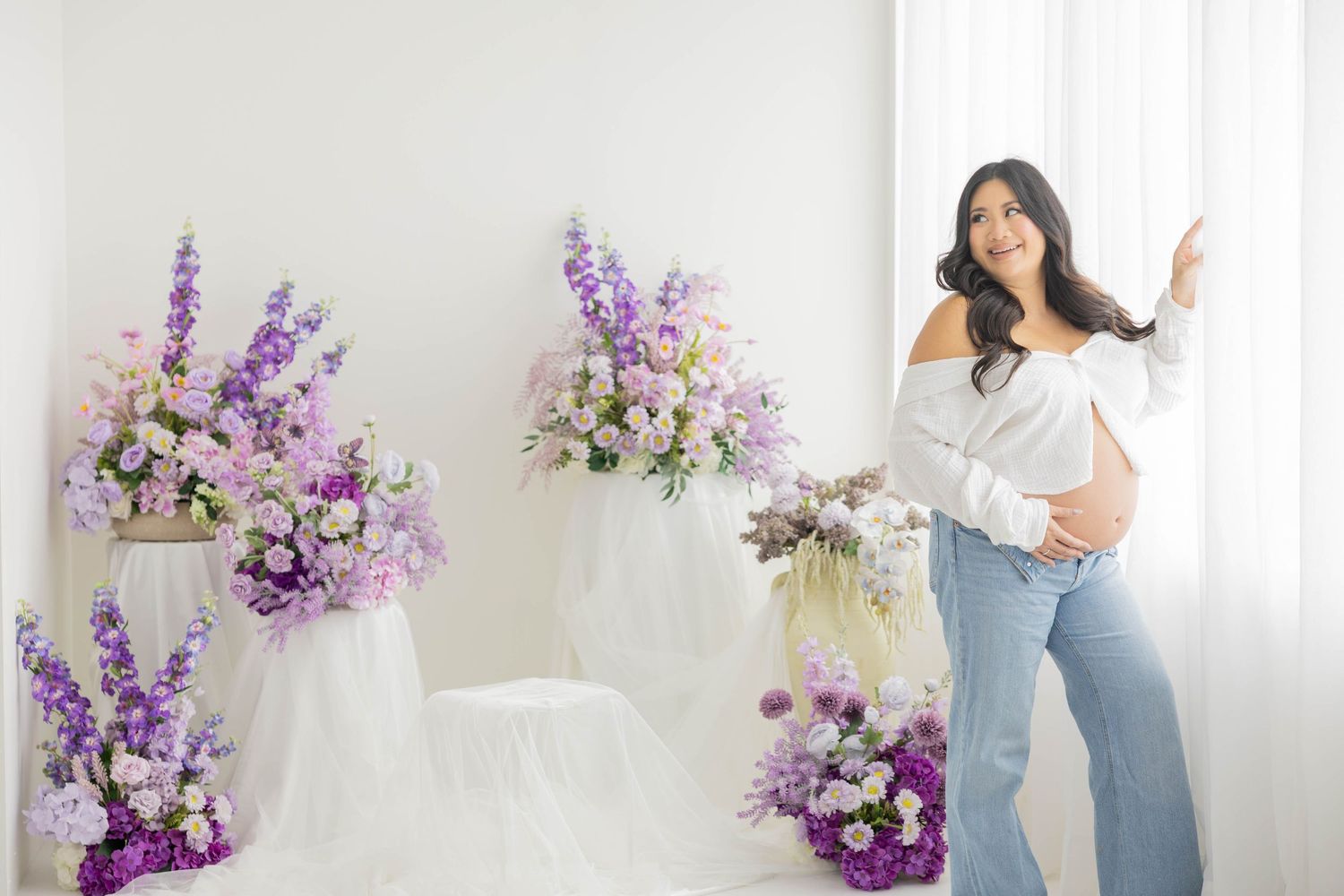 A bright studio photoshoot setup with purple and white floral arrangements against a white backdrop.