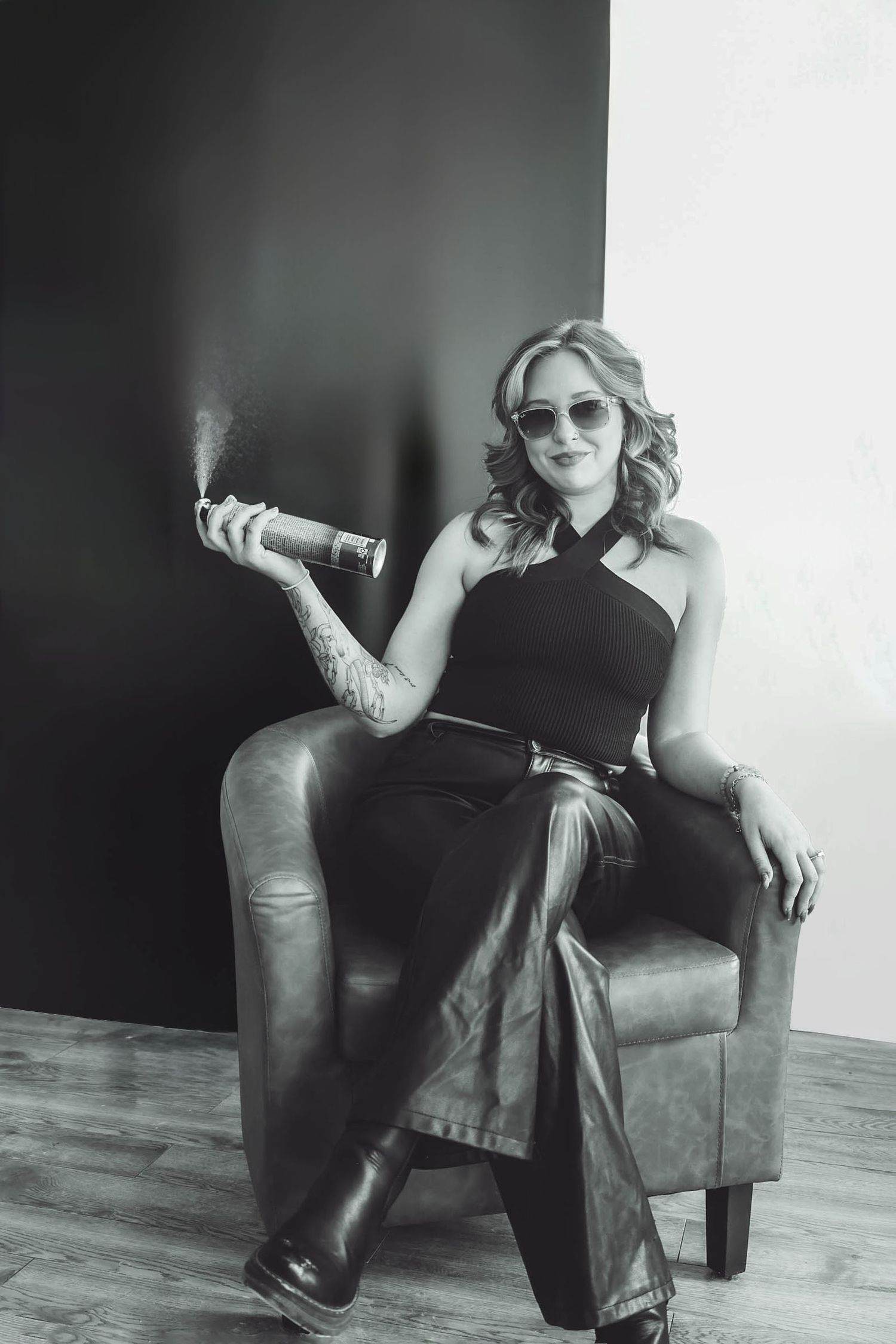 Stylish portrait of someone in sunglasses sitting in a leather chair with a curled hairspray mist for salon photography.