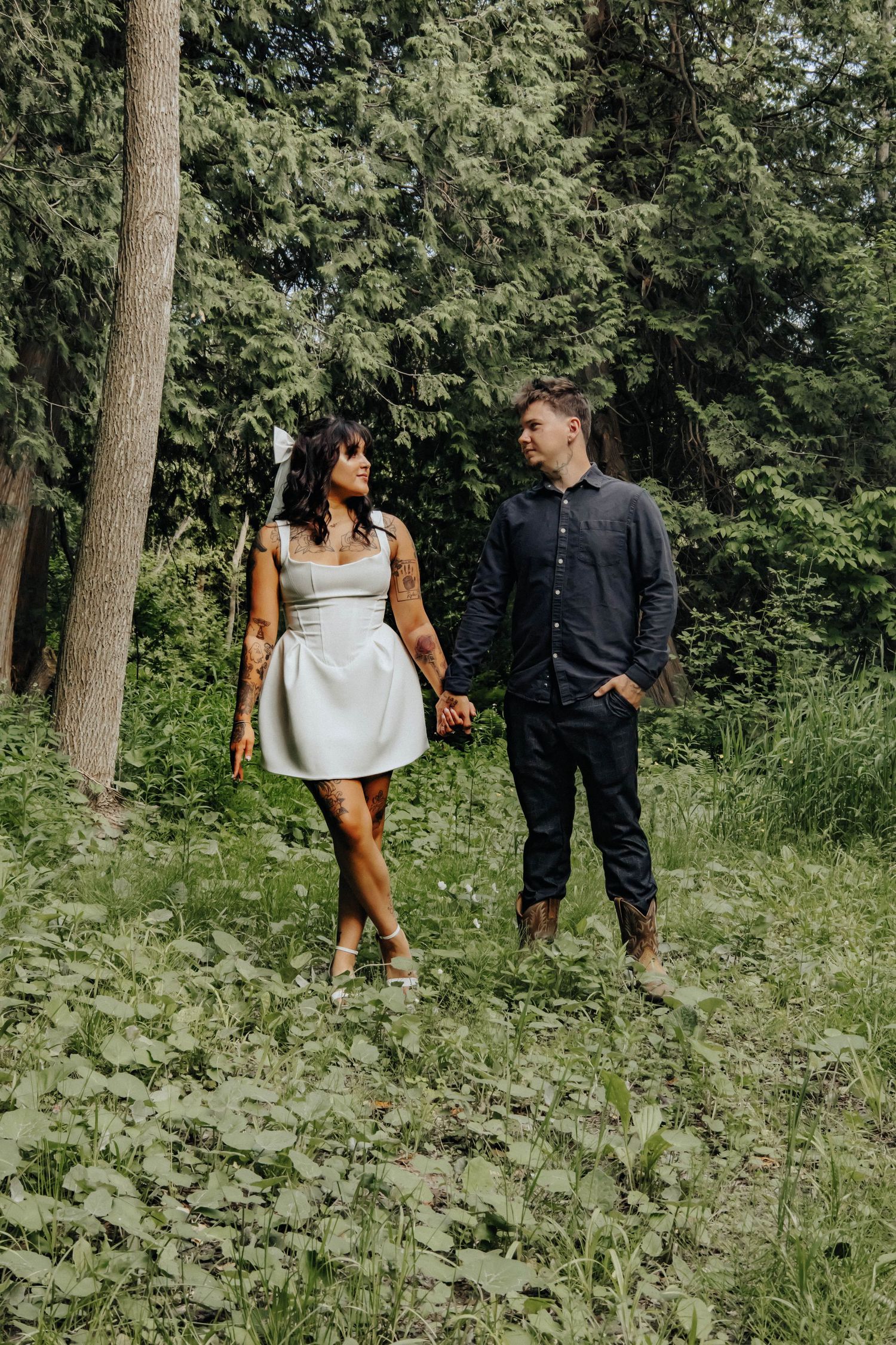 A couple shares playful moments together in a lush forest setting wearing contrasting outfits.