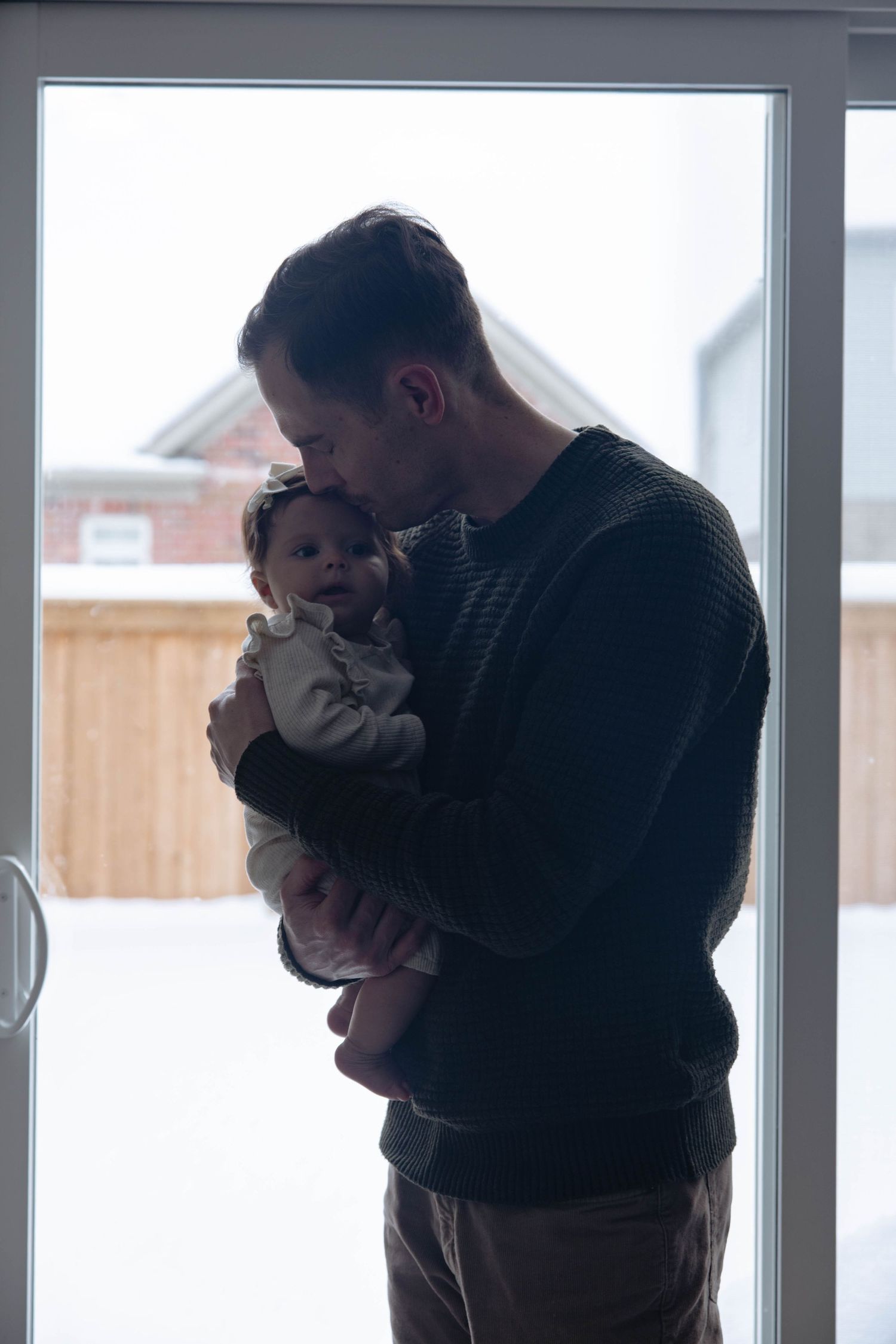 A tender moment between parent and baby silhouetted against a bright window in a cozy home setting.