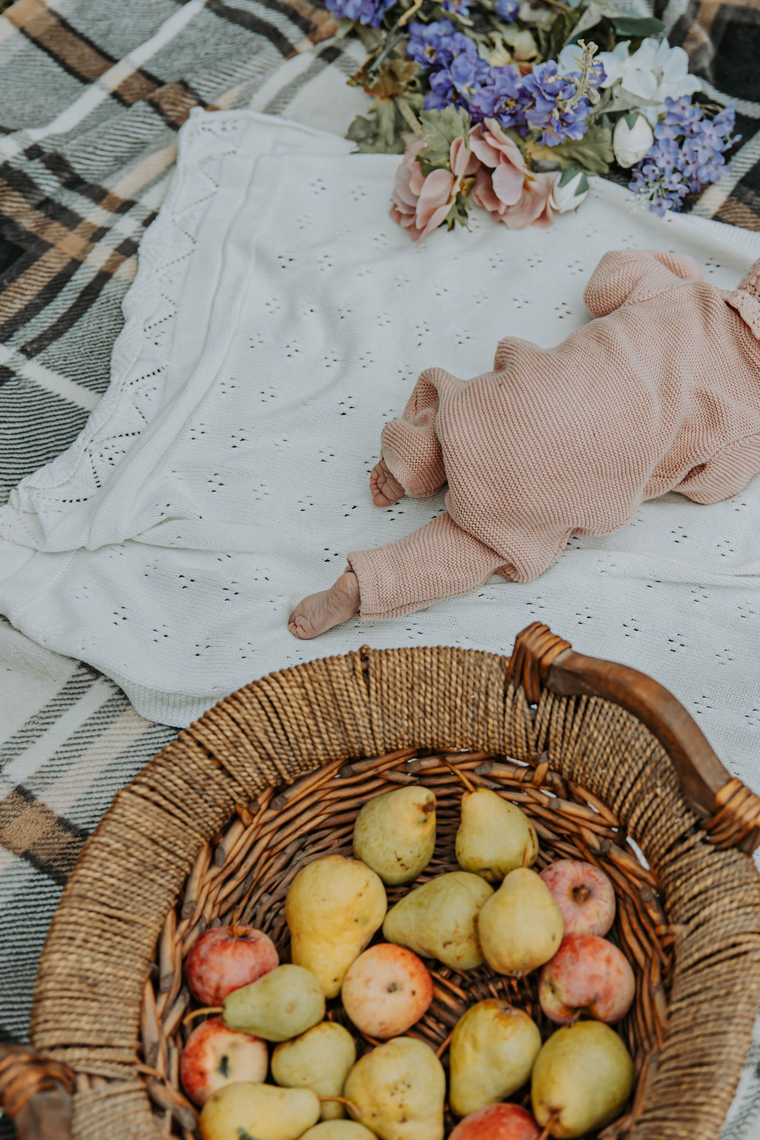 Fresh pears and apples in rustic woven basket with flowers and linen fabric on textured background.