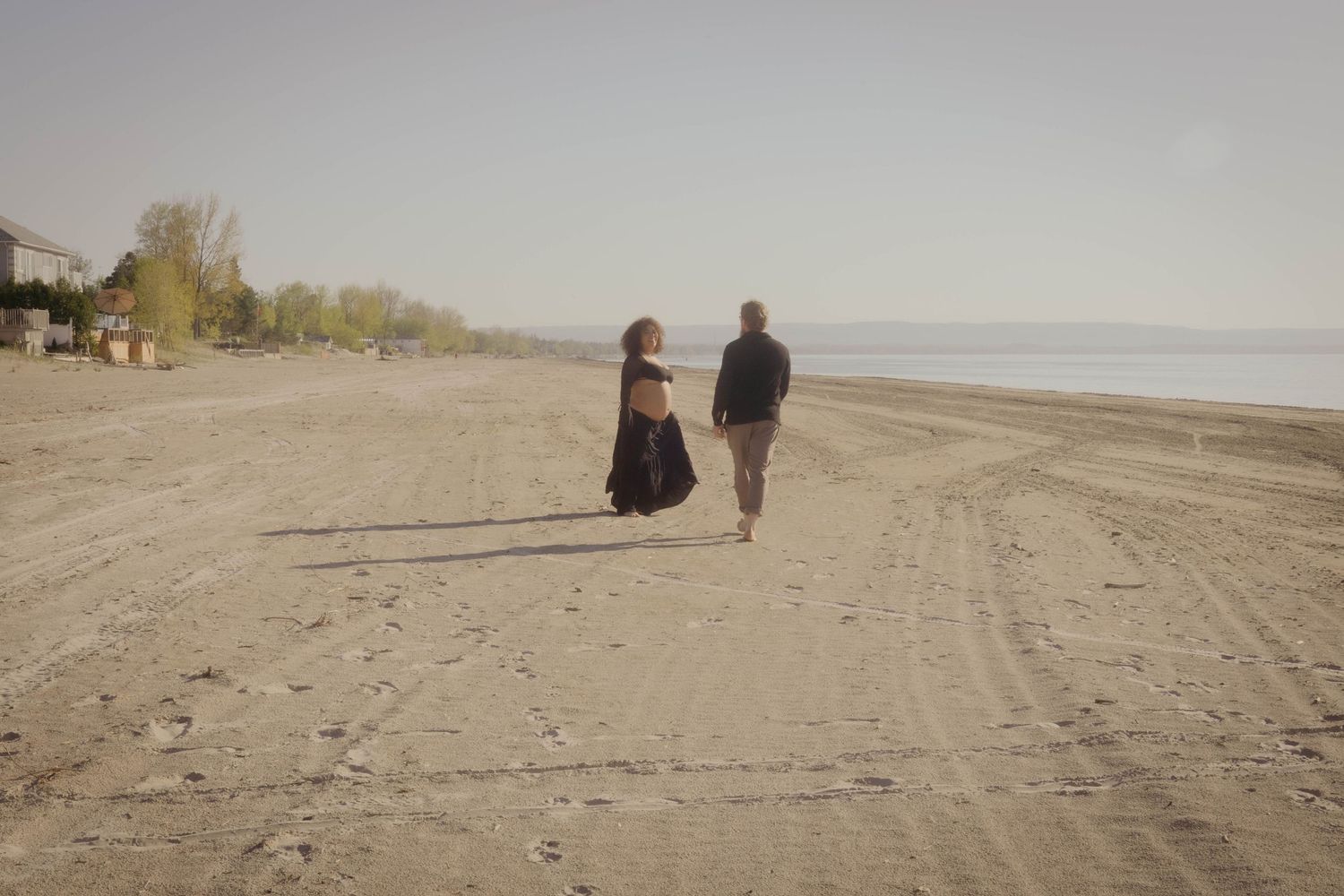Two people stroll together along an empty sandy beach on an overcast day.