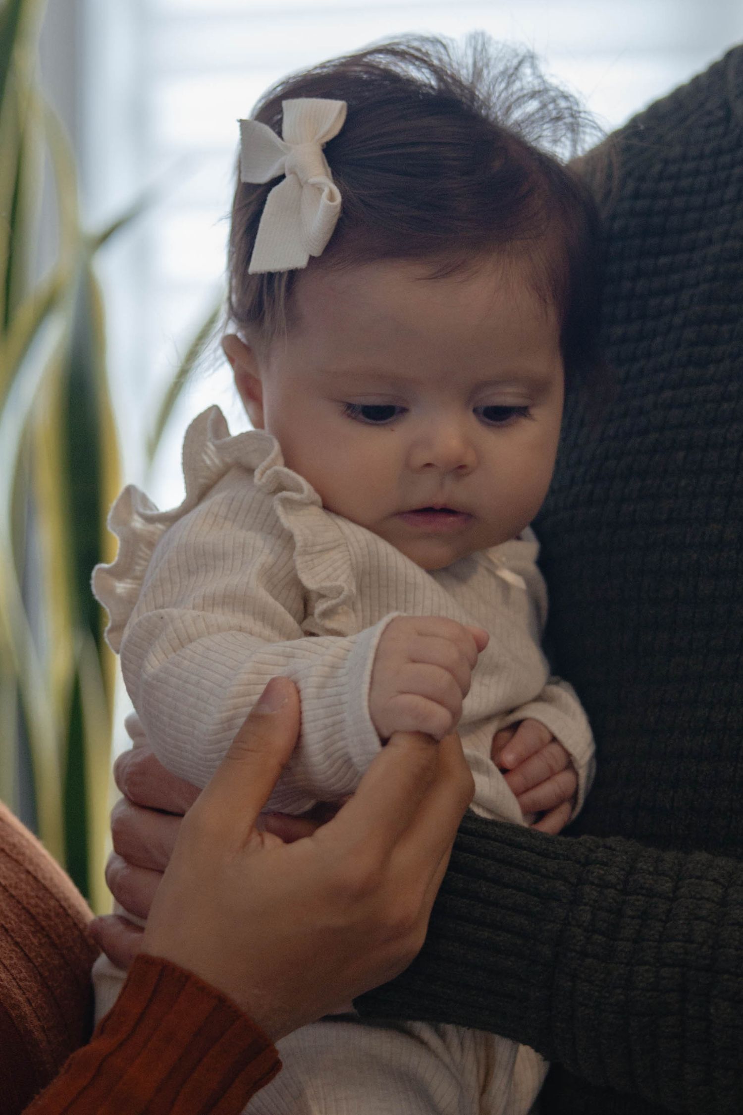 A small baby in white clothing makes adorable expressions while being held against a dark background.