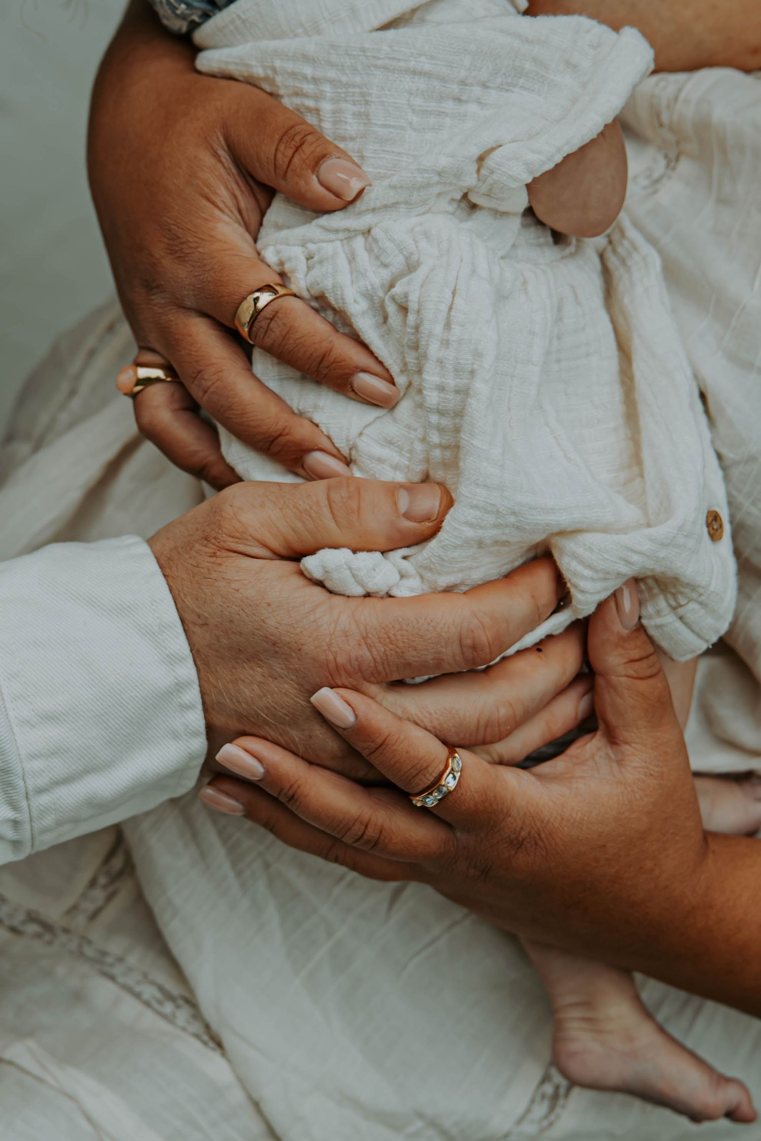 Close-up view of gentle hands holding and touching a baby's tiny feet wearing white clothing.
