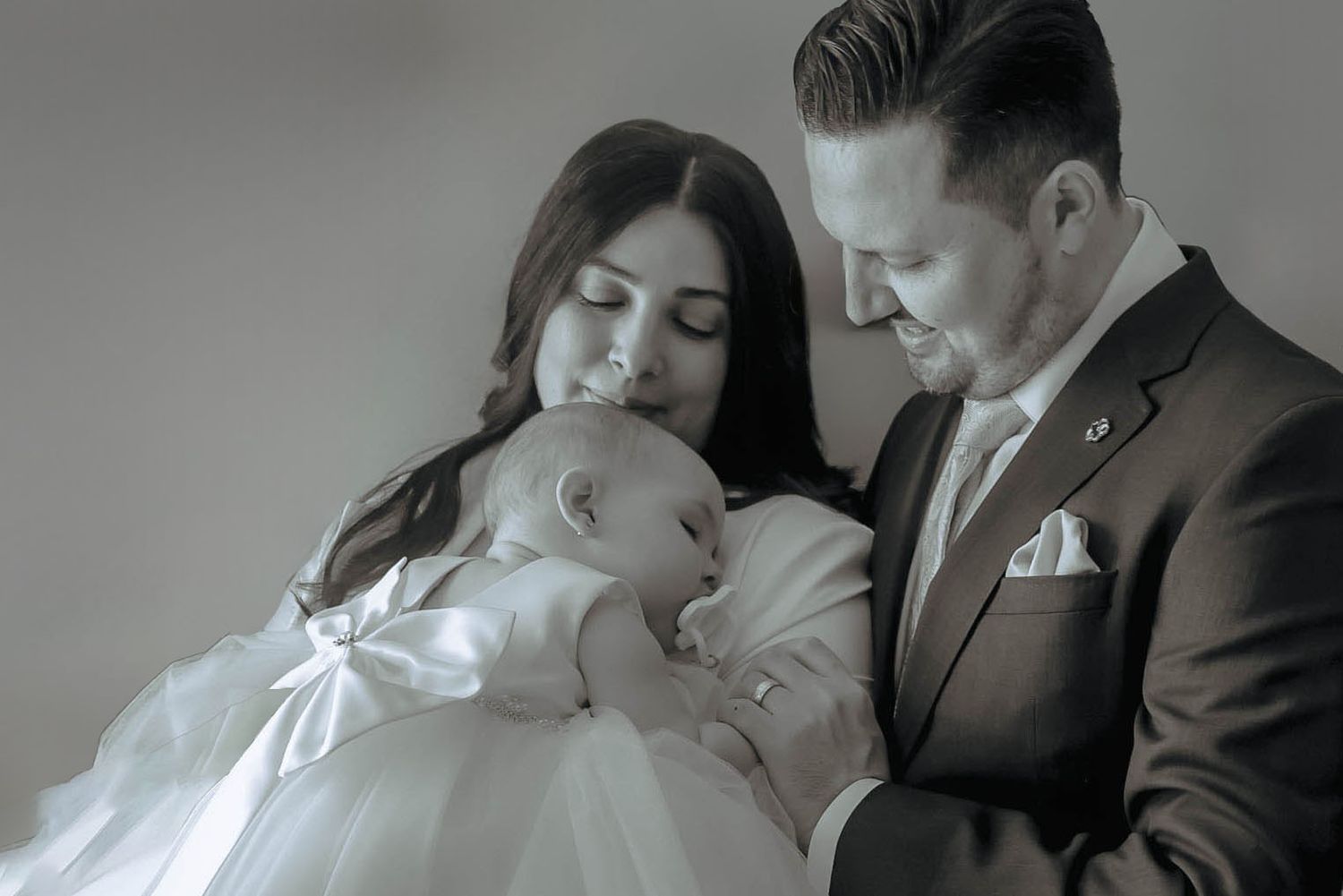 An intimate family portrait with a baby in white against a neutral backdrop.