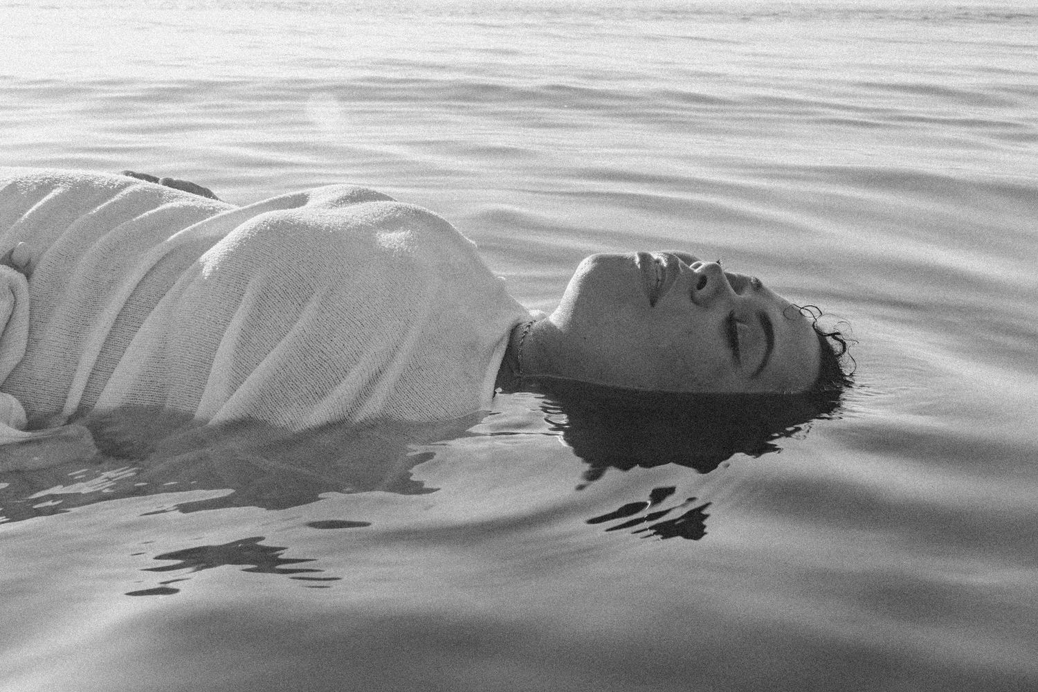 Black and white image showing a figure floating peacefully in rippling water.