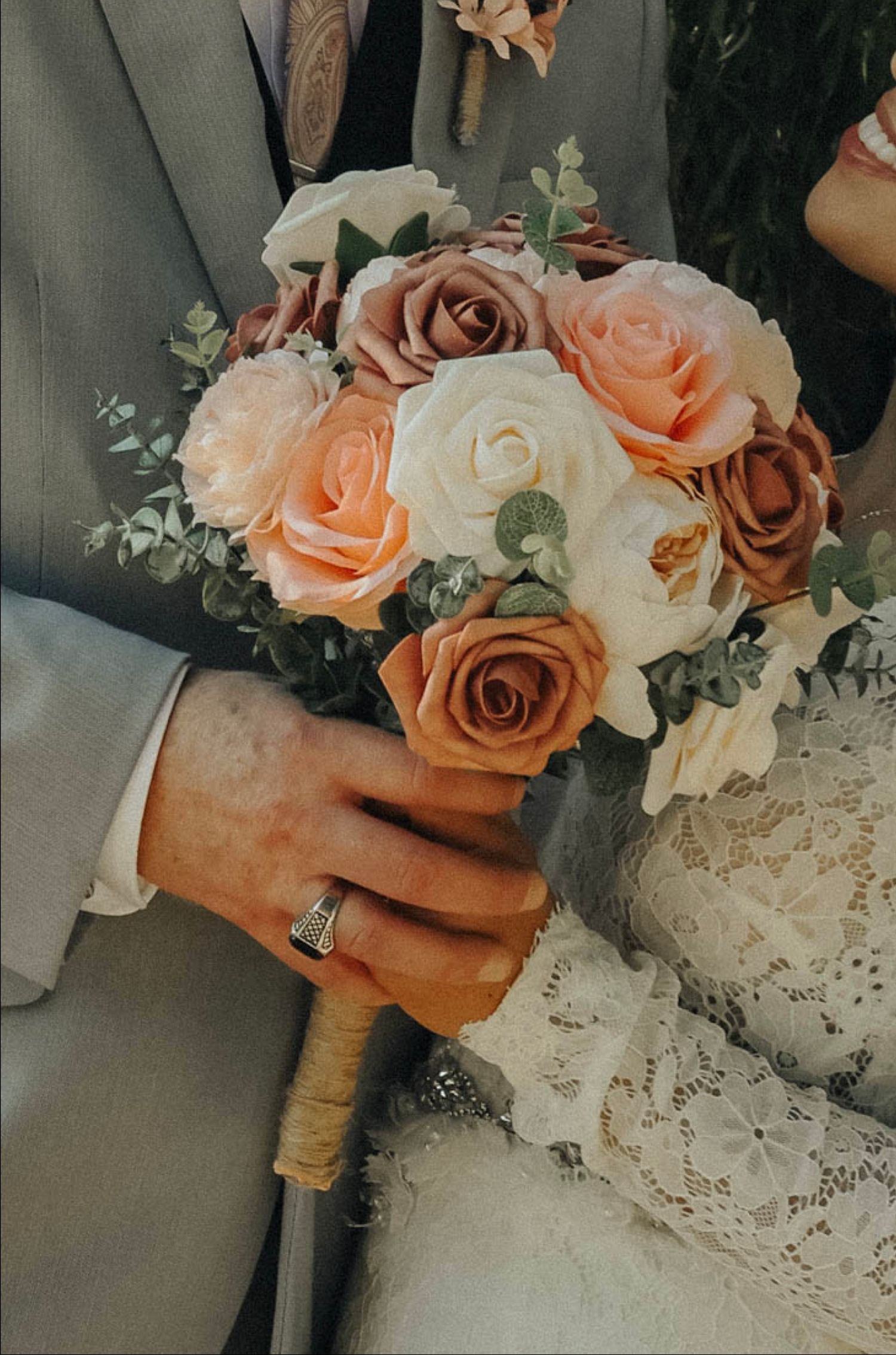A romantic wedding bouquet featuring peach and cream roses with eucalyptus leaves wrapped in a rustic burlap handle.