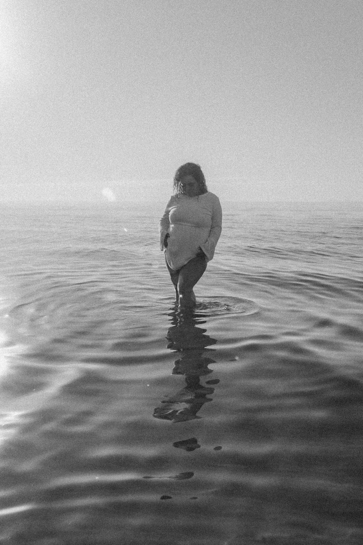 Black and white photo of a person standing in rippling ocean water.