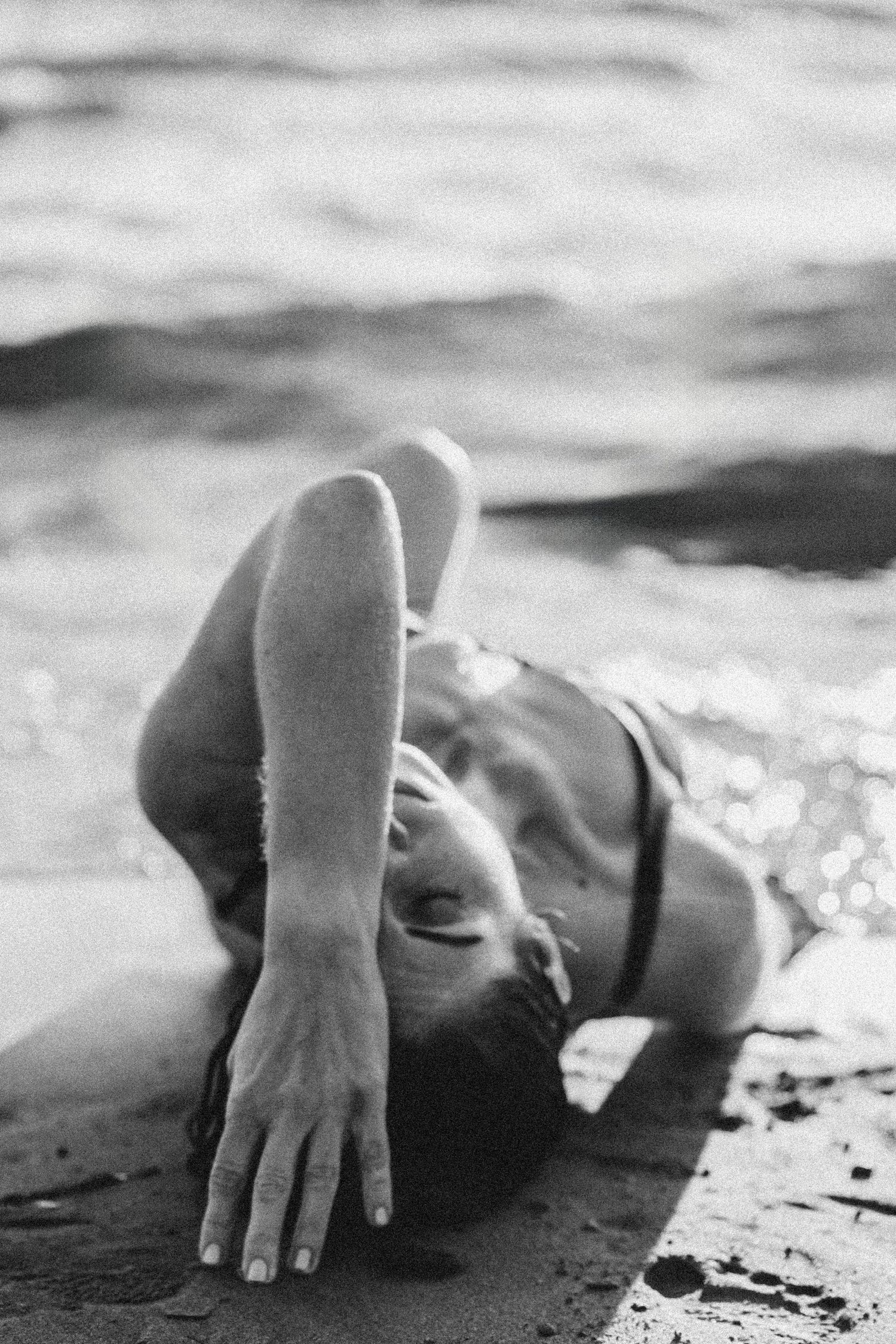 Artistic black and white portrait of someone lying on a beach with waves in the background.