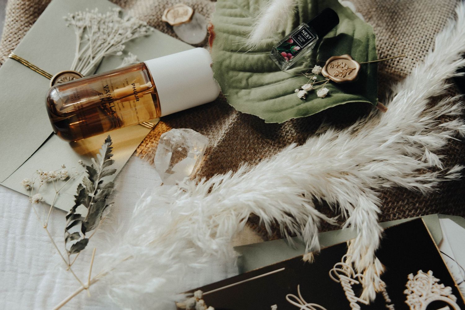 Flatlay of essential oils, dried flowers, feathers and natural wellness items arranged on rustic wooden surface.