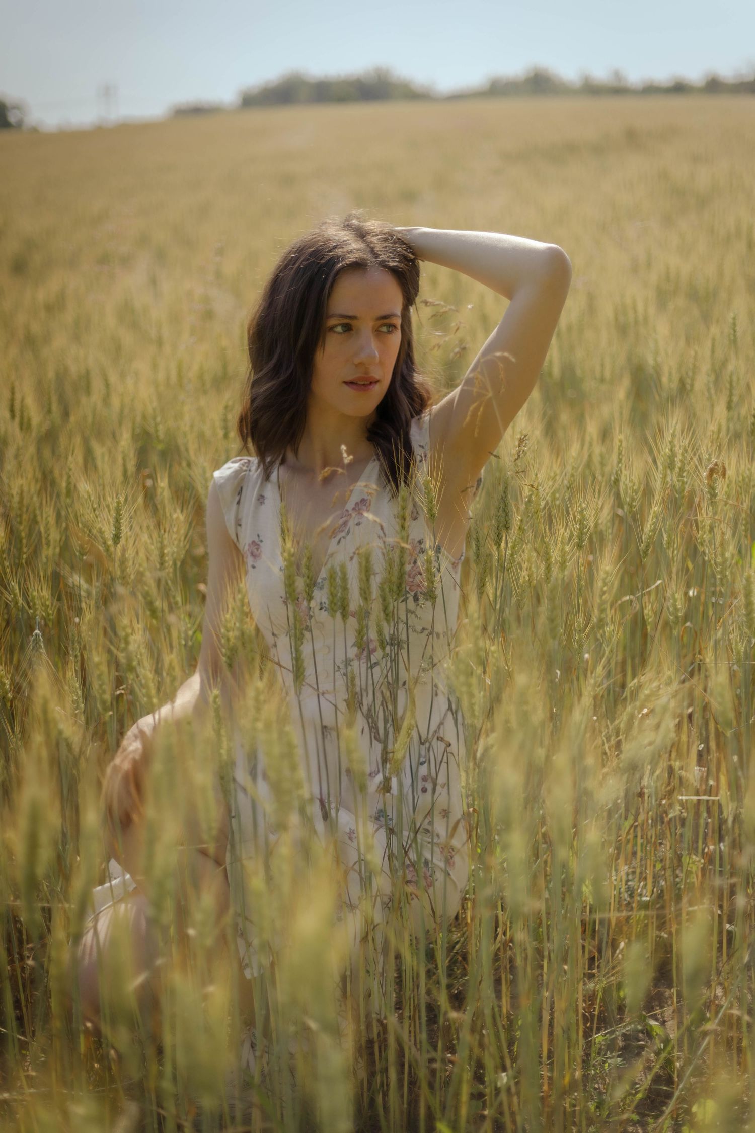 Person in white dress poses gracefully in golden wheat field during sunset.