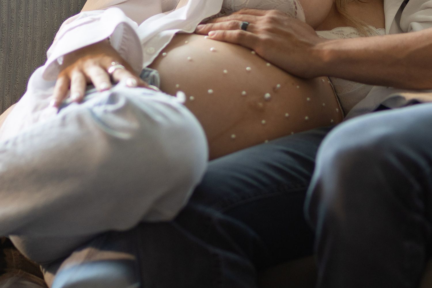 Couple sharing tender moment with hands on pearl-decorated pregnant belly, sitting together.