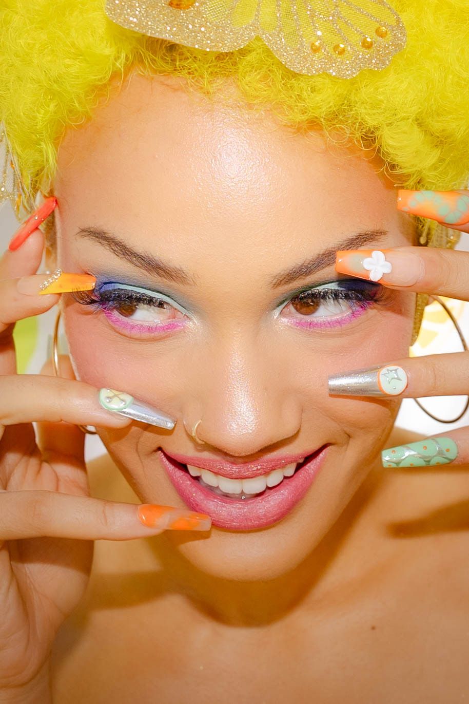 Close-up beauty shot with yellow wig and colorful makeup against citrus-patterned background.