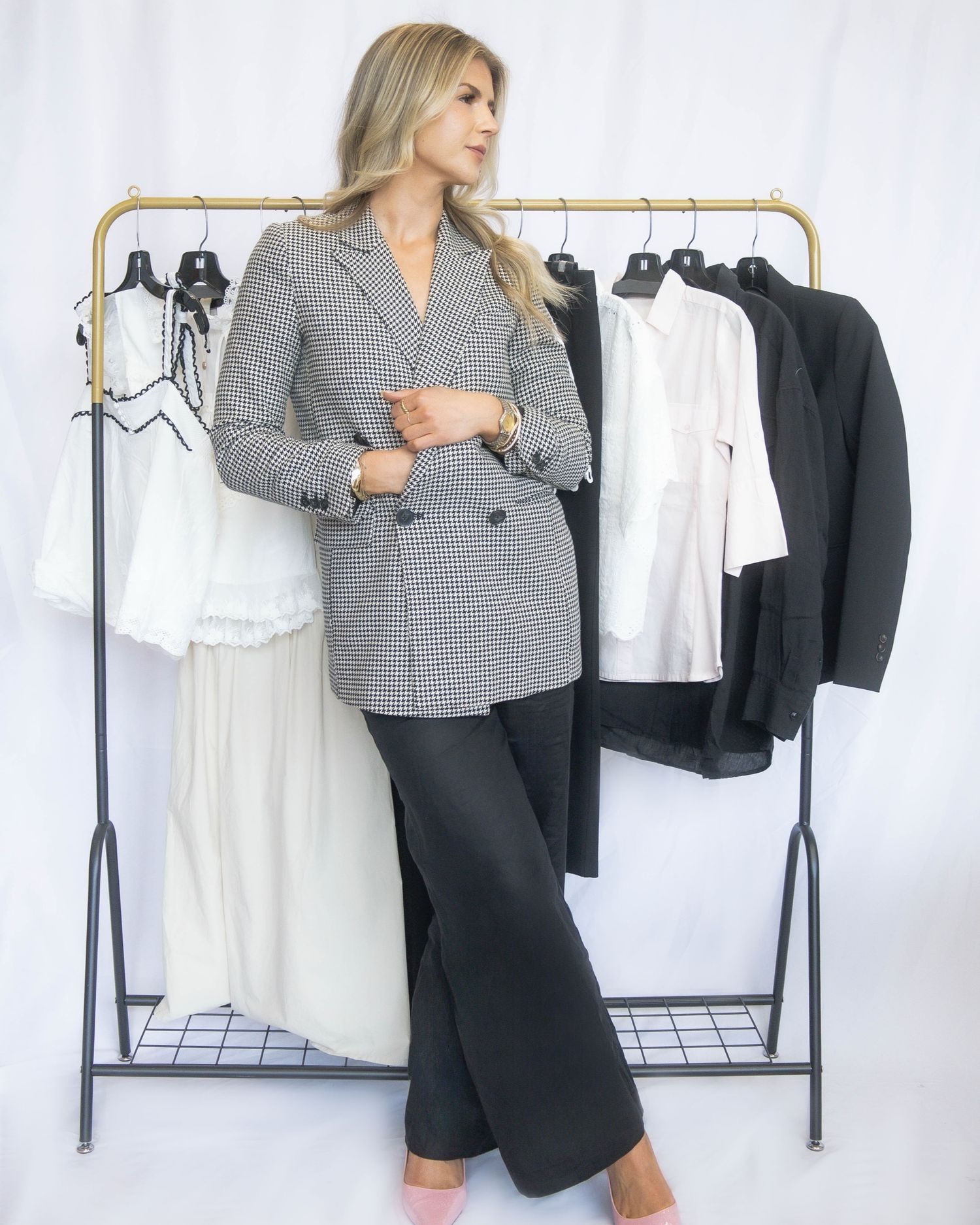 Fashion model in grey plaid blazer and black pants poses near clothing rack with white and black garments.