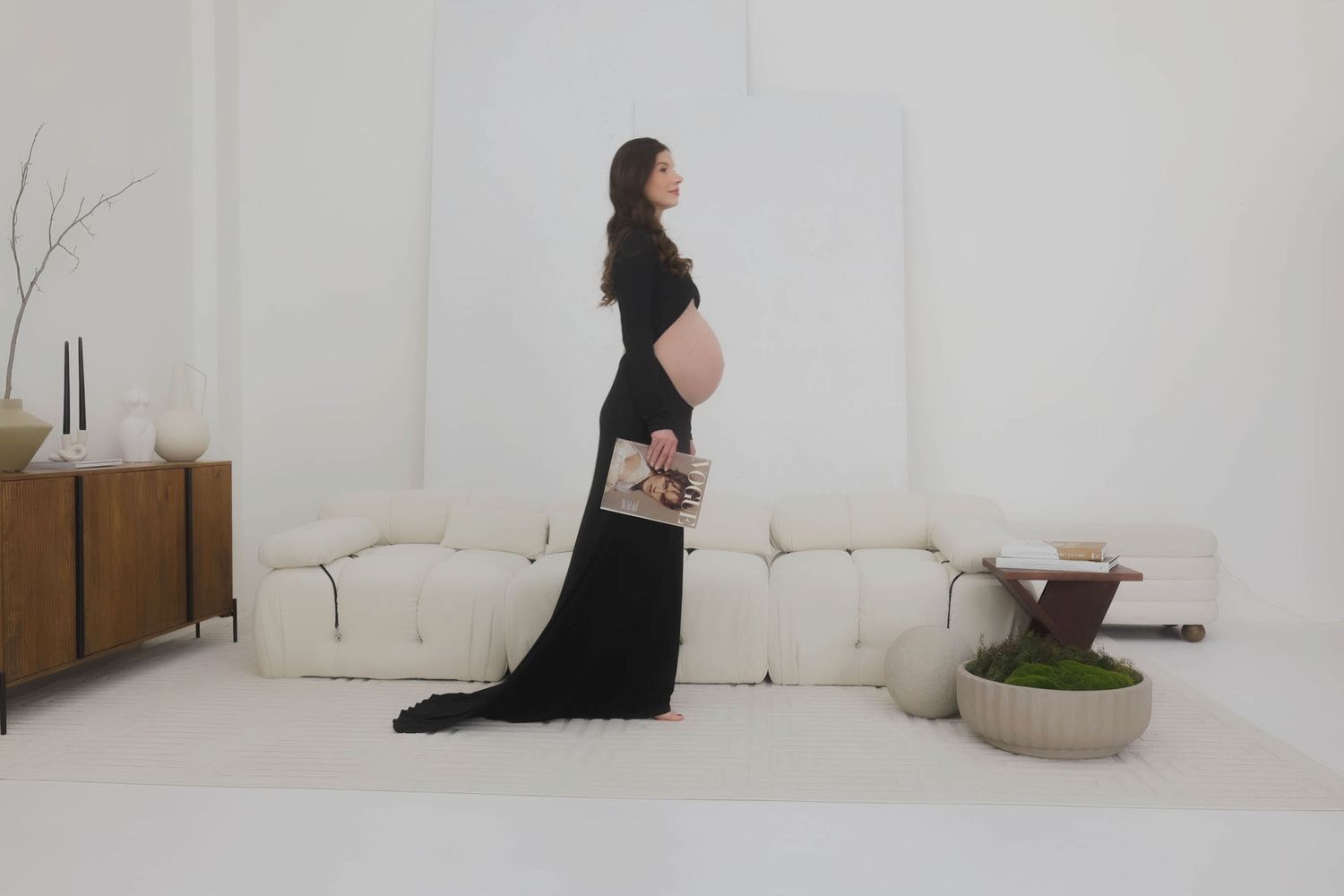 Side profile maternity photo with flowing black dress against white minimalist background.