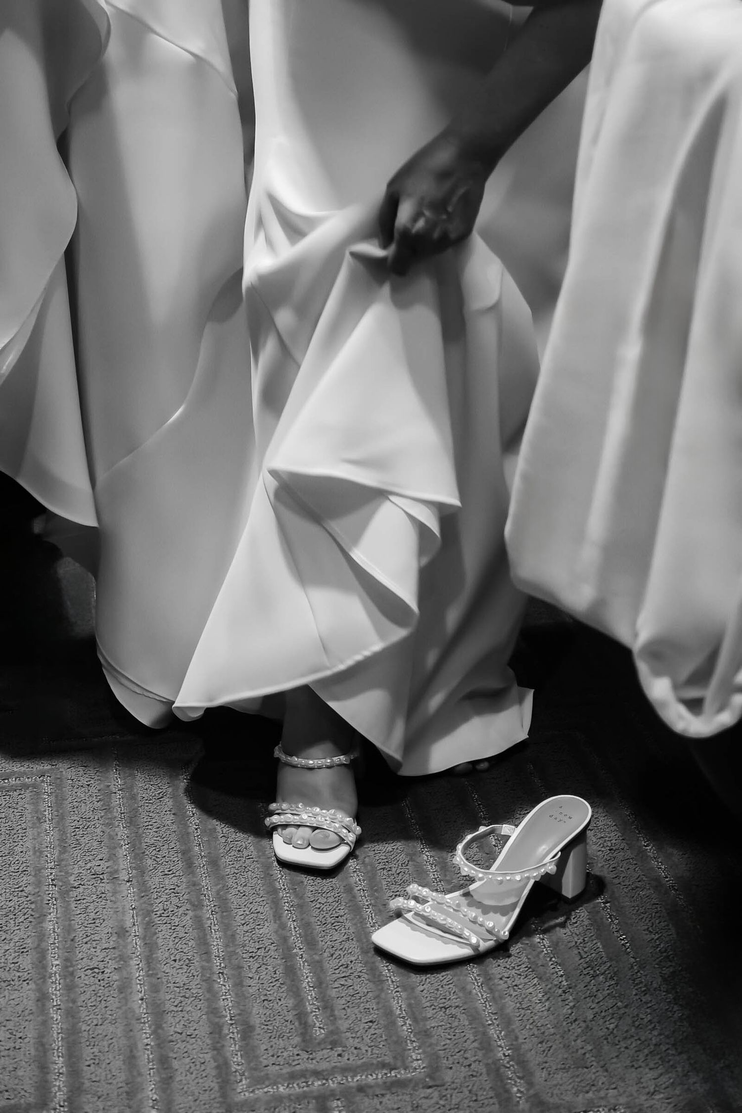 Detail shot of bridal shoes and dress hem on carpeted floor.