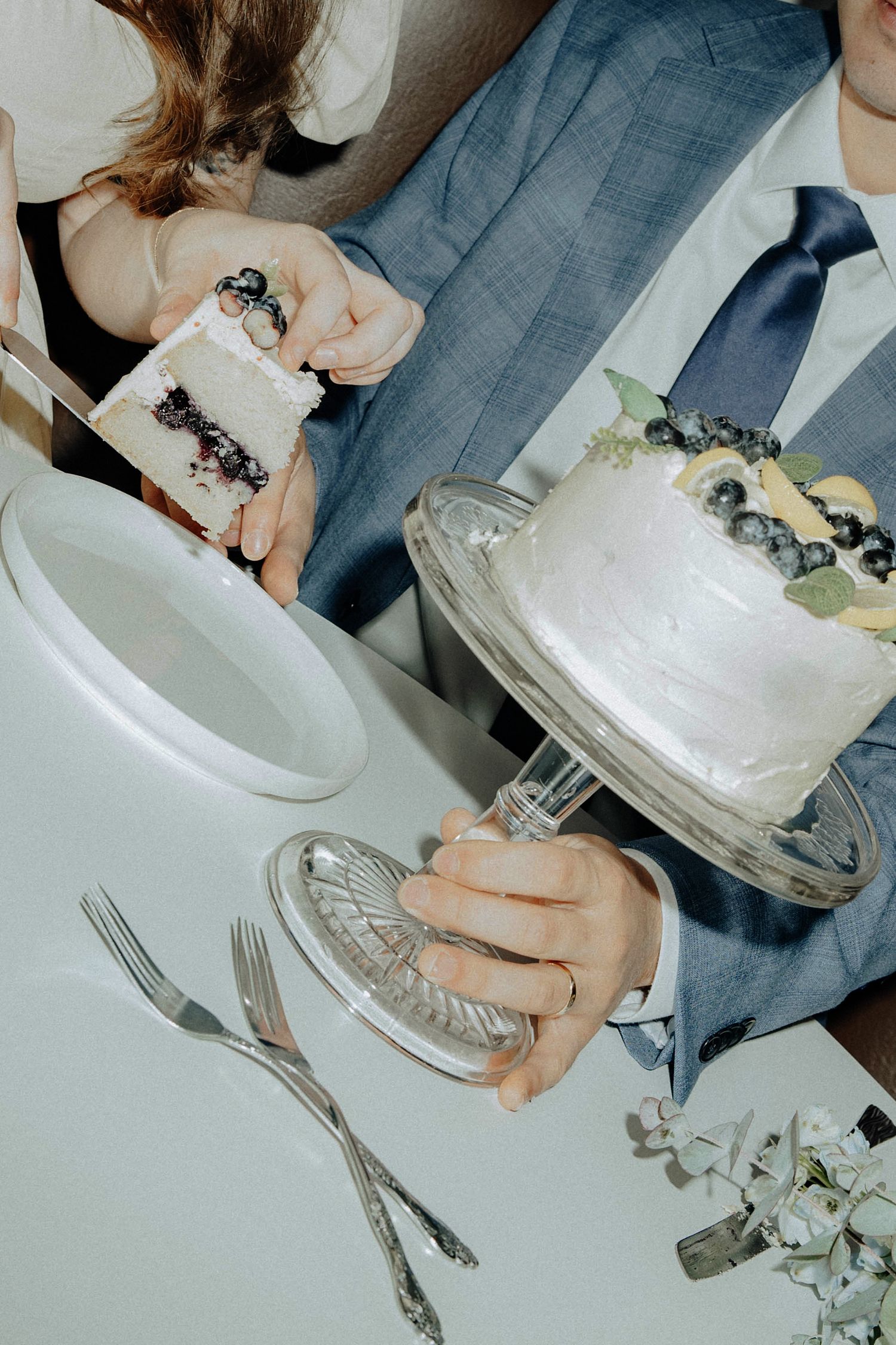 Wedding guests sharing slices of a white frosted cake at a reception table.
