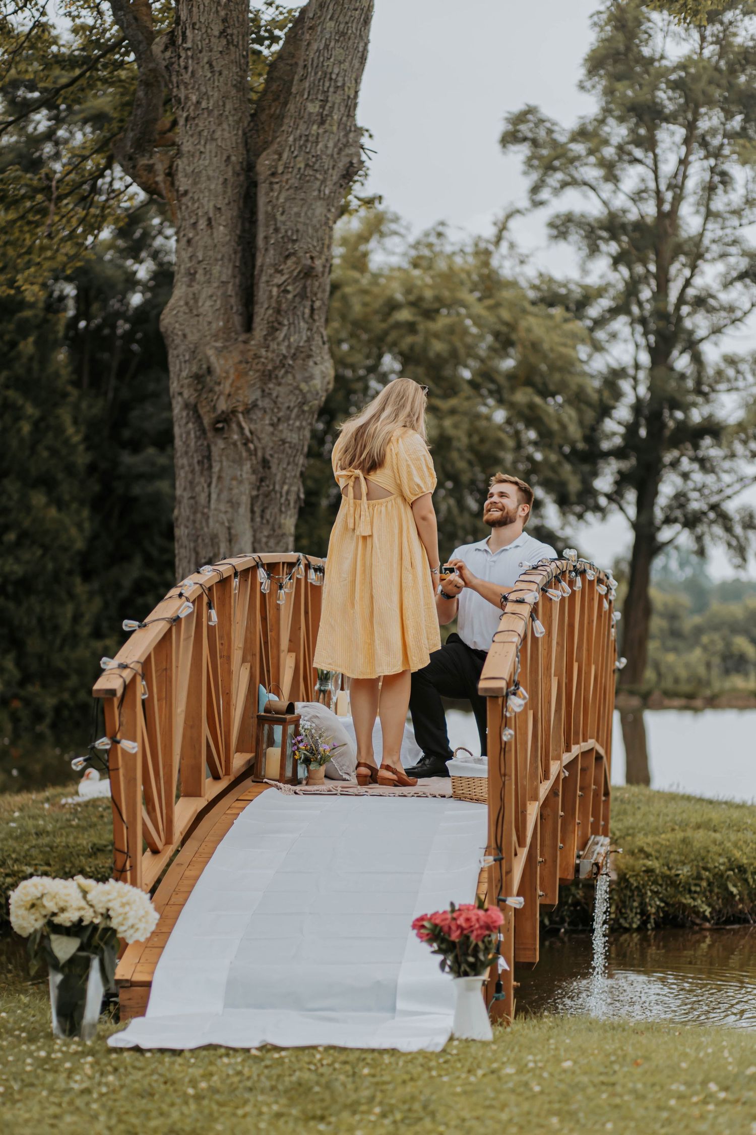 Wooden bridge railing by a lake with pink flowers visible in the foreground.
