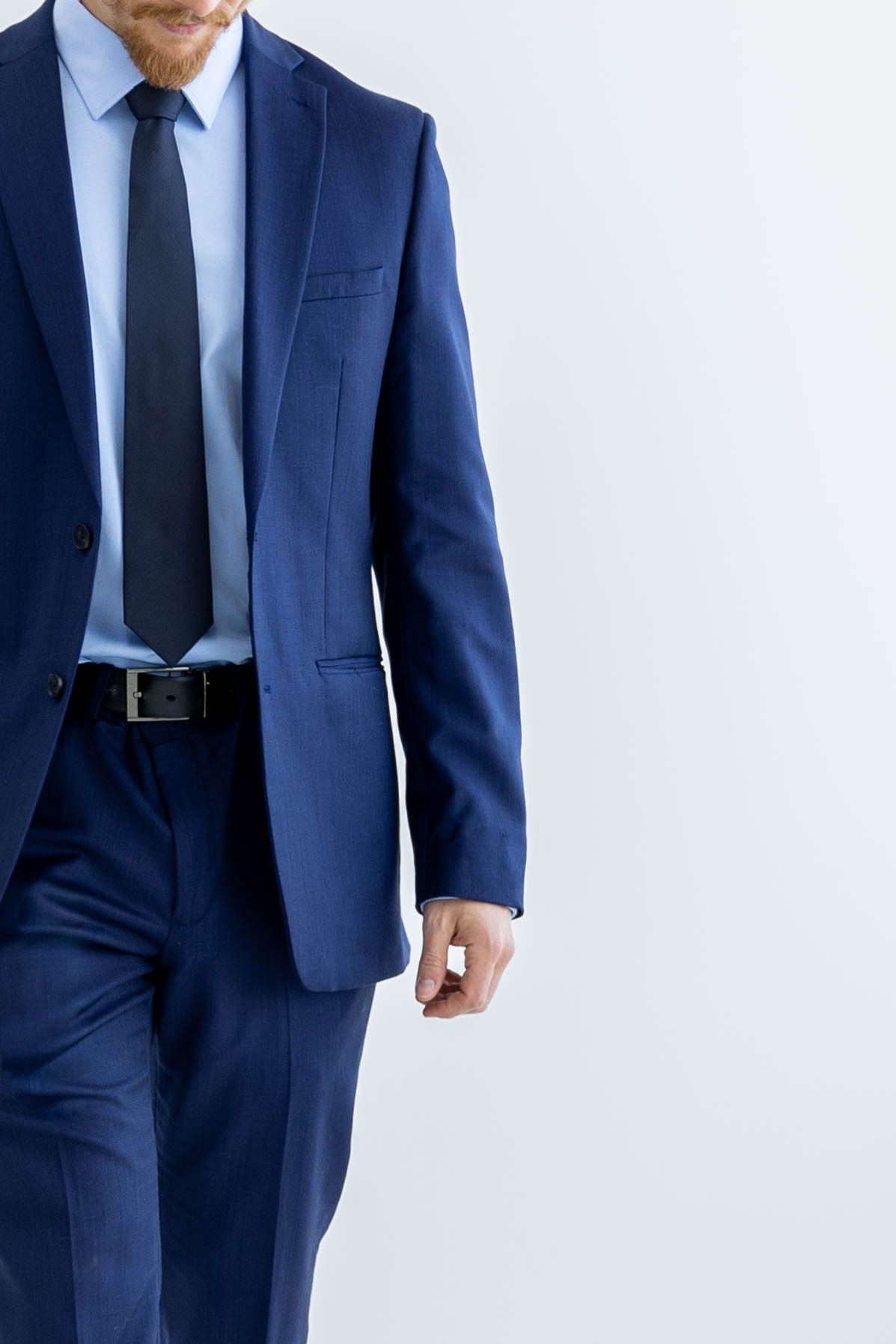 Professional wearing a tailored navy blue suit with black tie stands against white background.