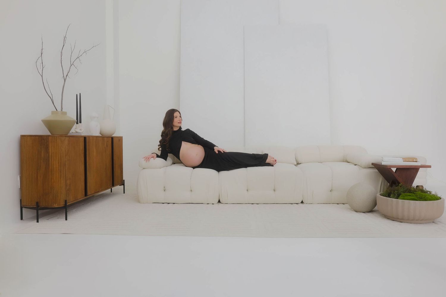 Artistic maternity portrait with a lounging pose on a white couch next to wooden furniture.