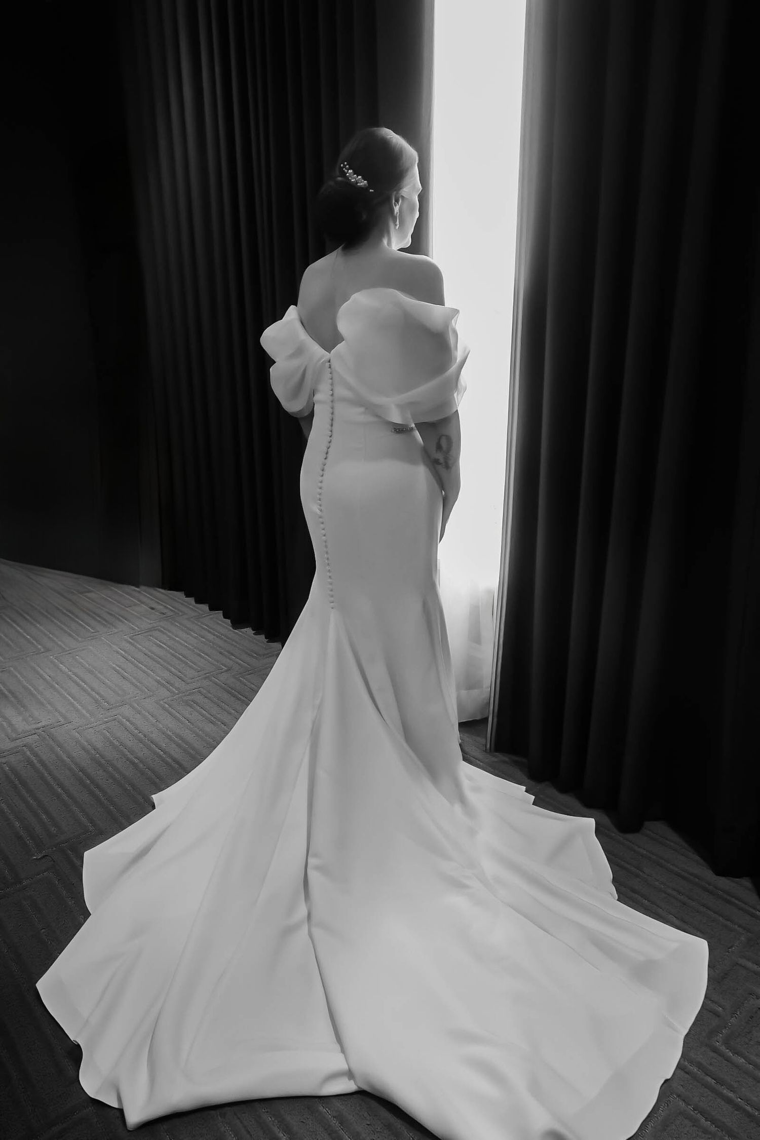 Dramatic black and white photo of bride in fitted wedding dress with bow detail and flowing train.
