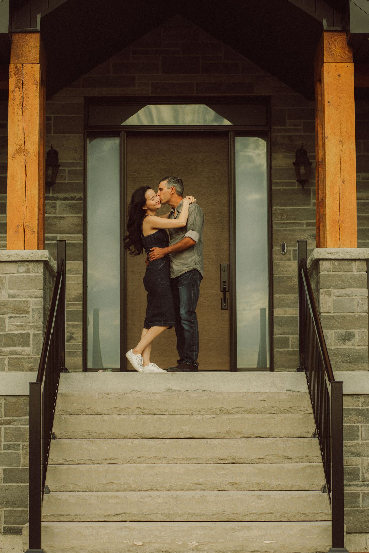 Romantic couple kissing on stone steps at the entrance of an elegant home with wooden accents.