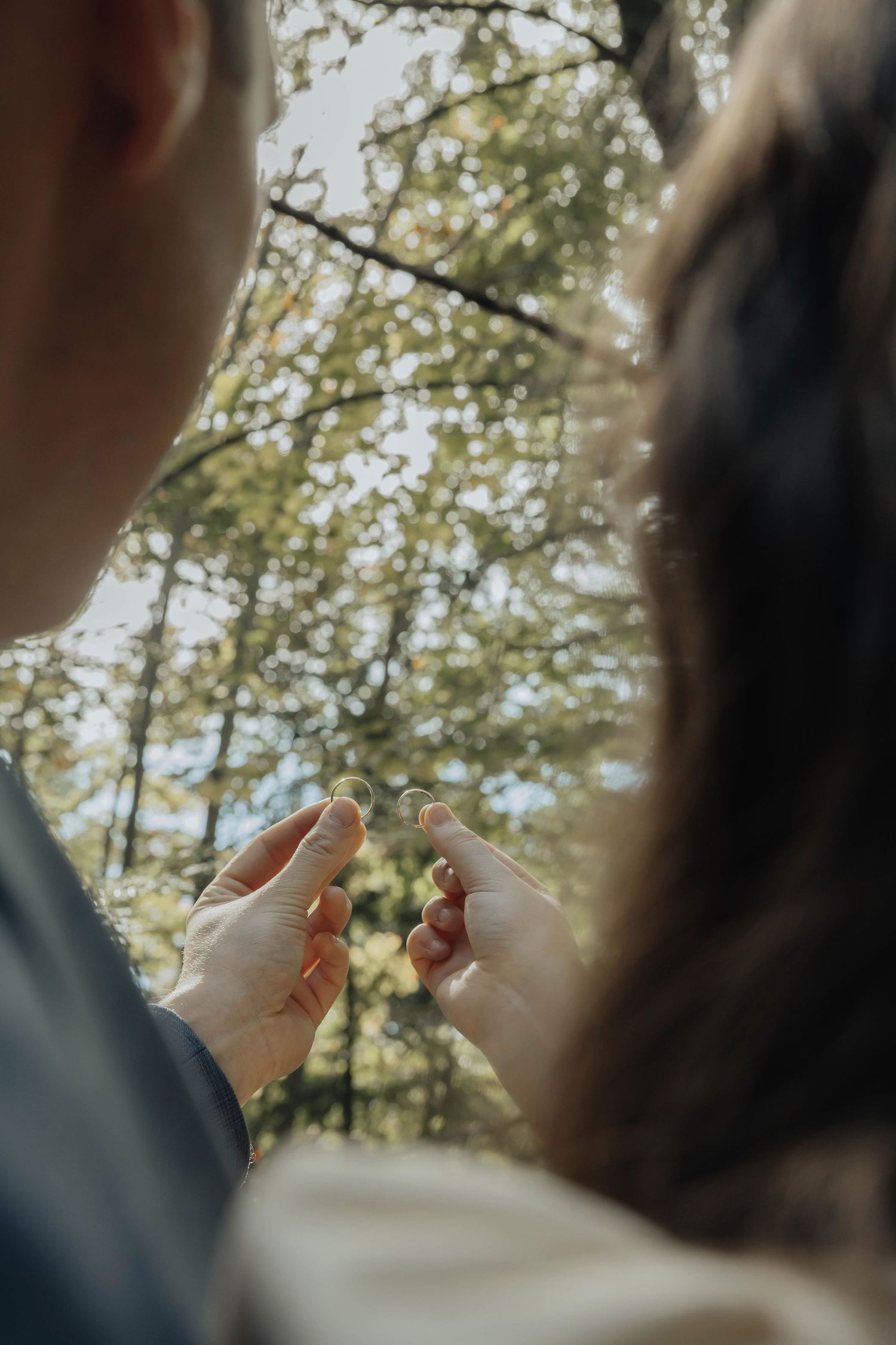 Close up of an intimate ceremony moment with sunlight filtering through trees in the background.