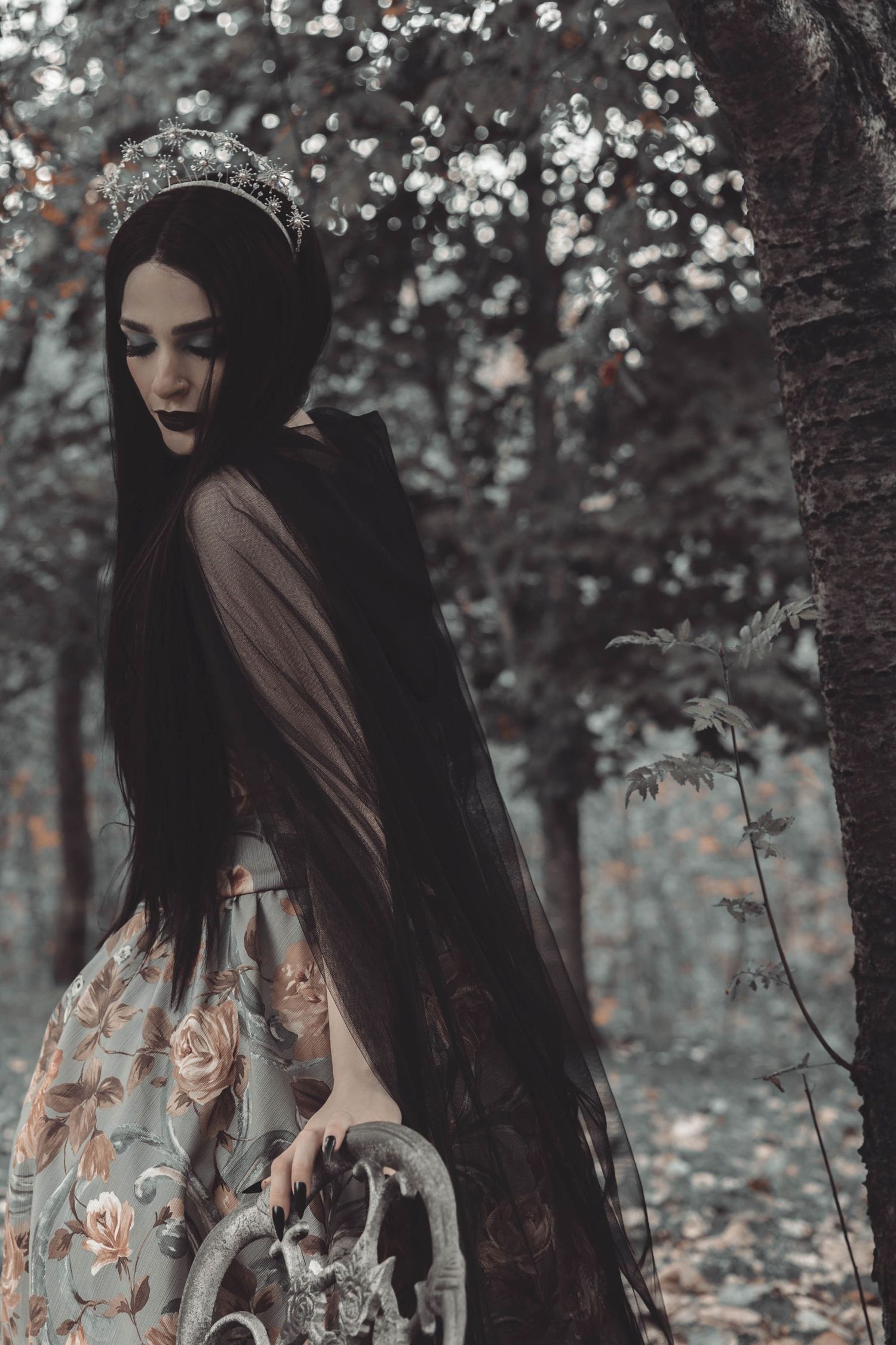 A figure in dark clothing and veil stands in a moody forest setting with soft lighting and muted colors.