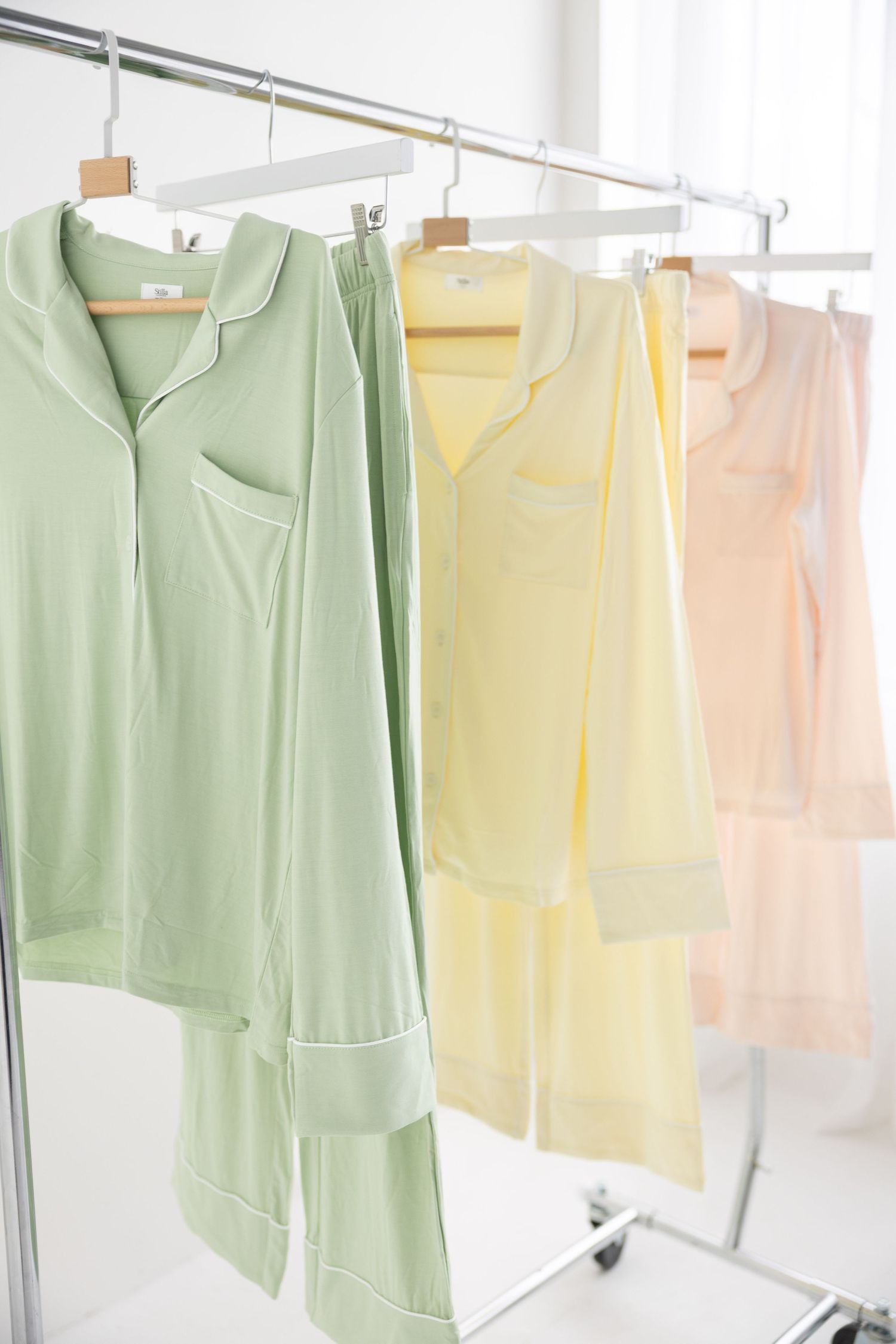 Pastel pajama sets in green, yellow, and peach hanging on a clothing rack in a bright white room.
