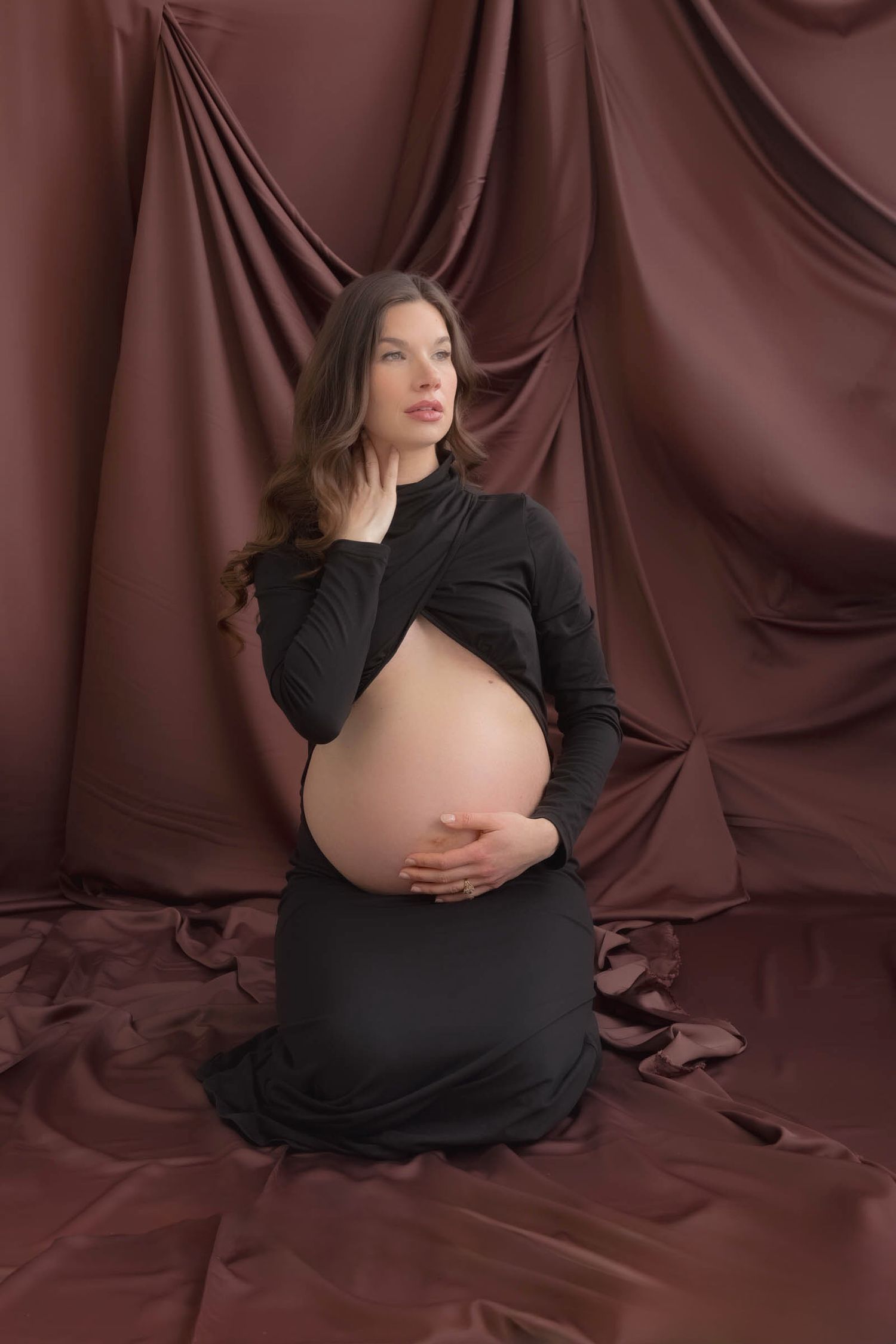 An elegant maternity portrait with brown draped fabric backdrop and black dress.