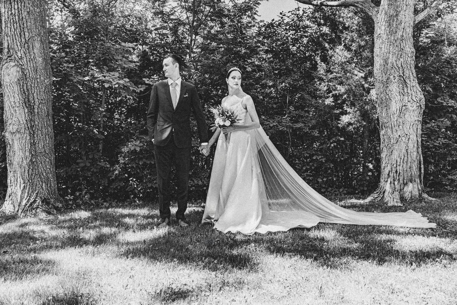 A classic black and white wedding portrait of a couple walking through a wooded garden.