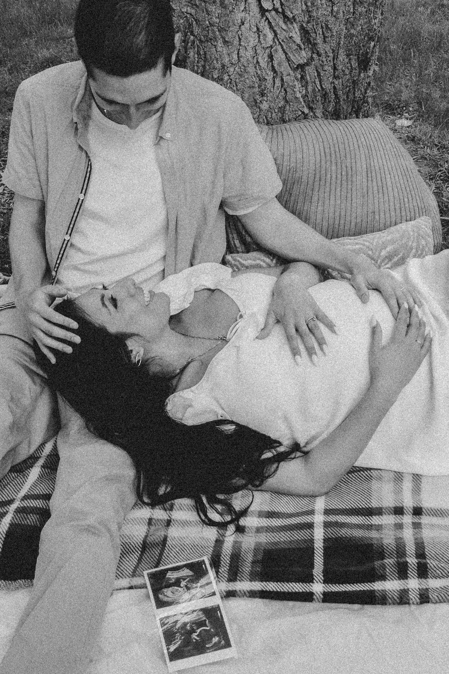 A black and white photo of a couple relaxing on a picnic blanket with ultrasound photos.