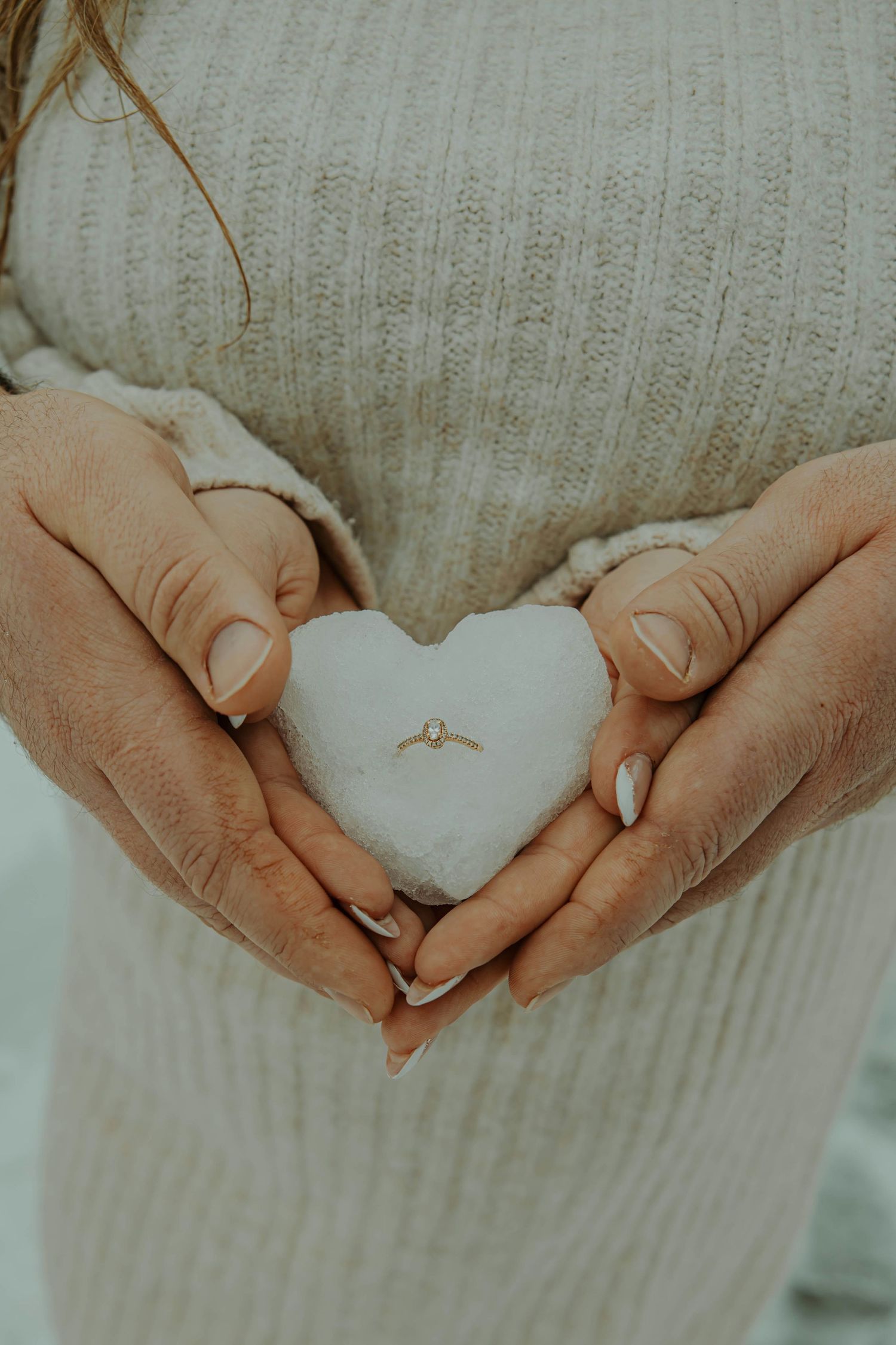 Hands gently holding and shaping a white heart-shaped object against a textured gray fabric background.