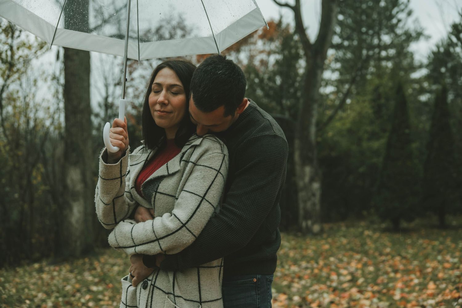 Romantic couple in warm clothing embraces outdoors during autumn with fallen leaves on the ground.