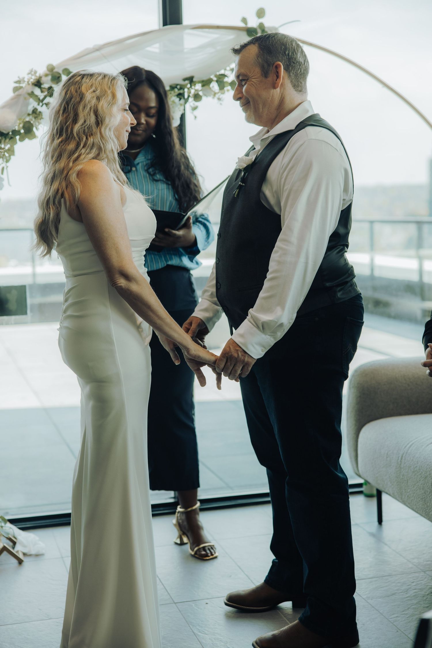 Bride and groom holding hands during intimate wedding ceremony with floral arch and officiant.