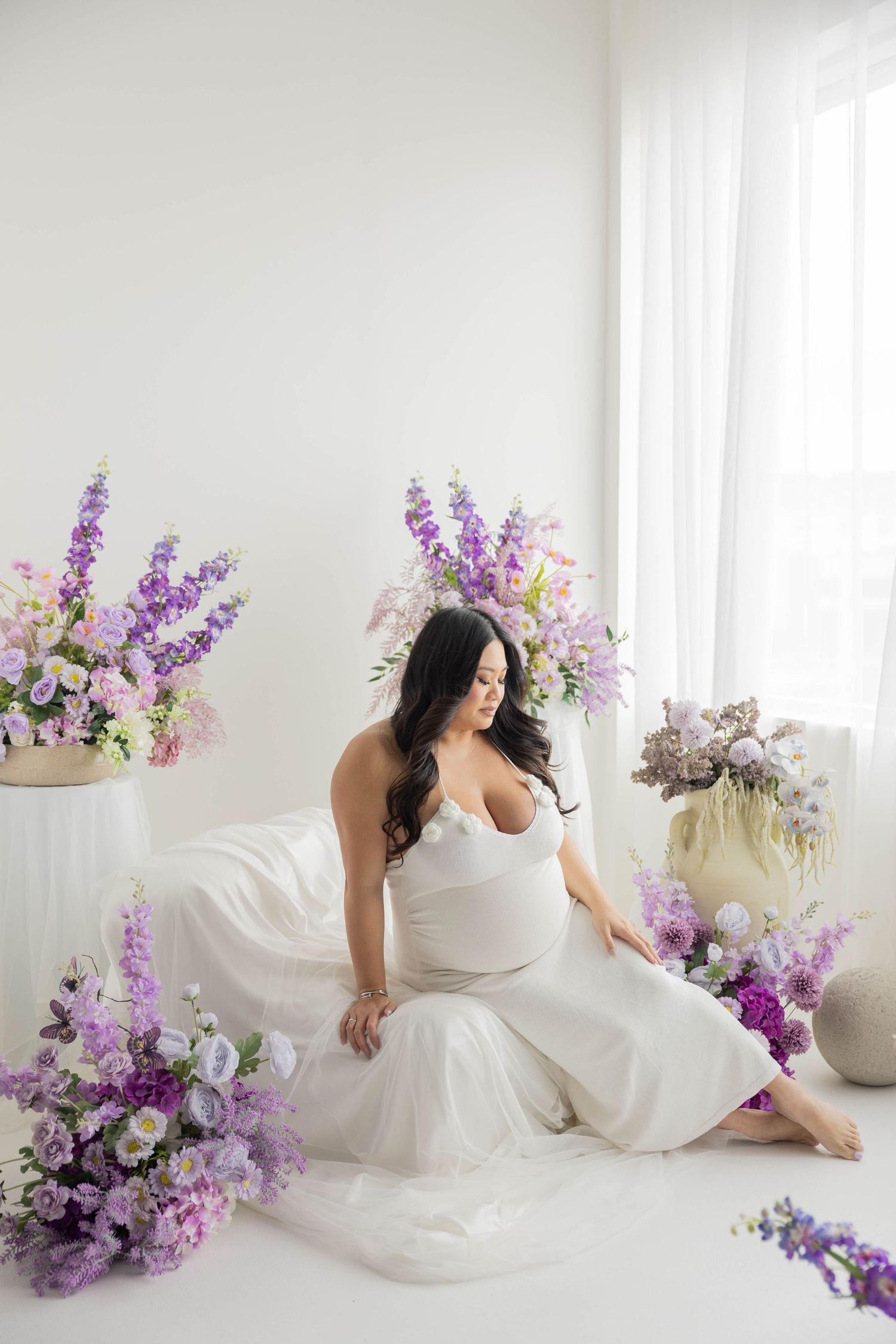 Dreamy boudoir session featuring flowing white fabric and purple flowers in a minimalist white room.