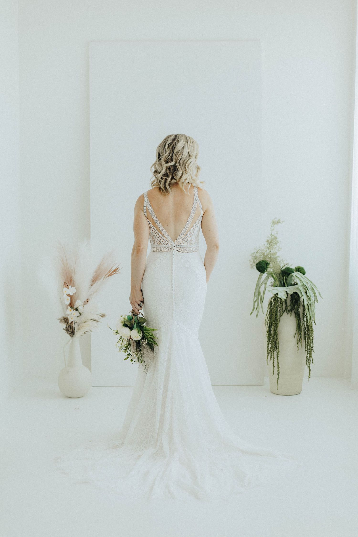Elegant white wedding dress with floral bouquet shown from different angles in bright minimalist room with vase.