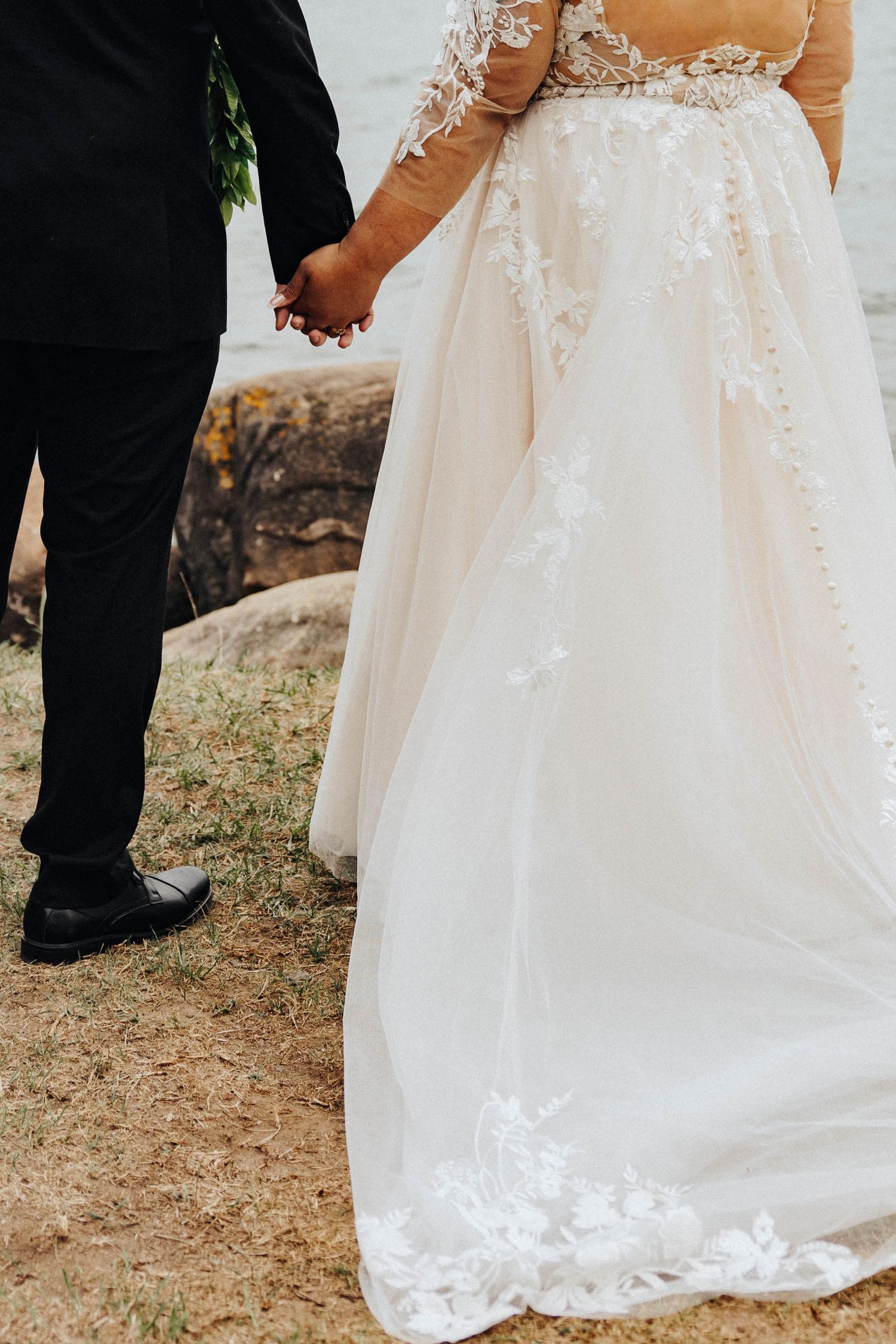 Close-up details of an elegant white bridal gown with delicate lace trim and embellishments at an outdoor wedding ceremony.