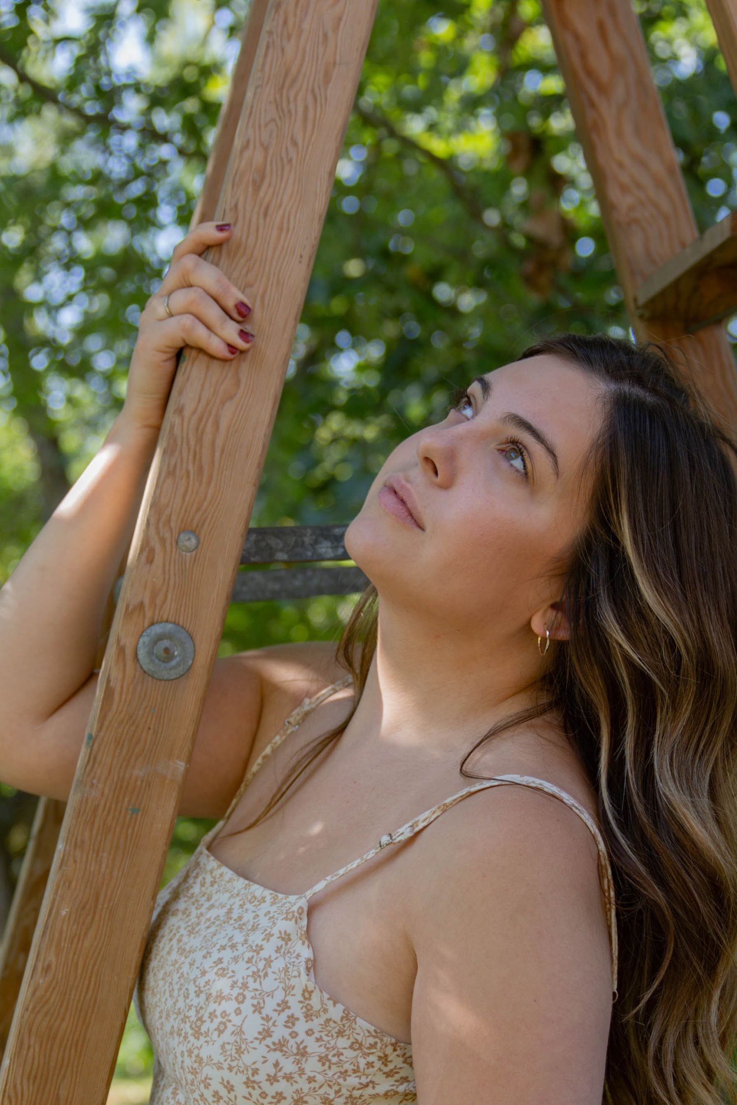 A figure poses thoughtfully against a wooden pergola post in natural outdoor lighting.