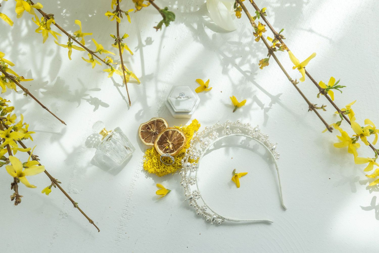 Glass perfume bottles with yellow forsythia flowers creating an elegant spring composition on white background.