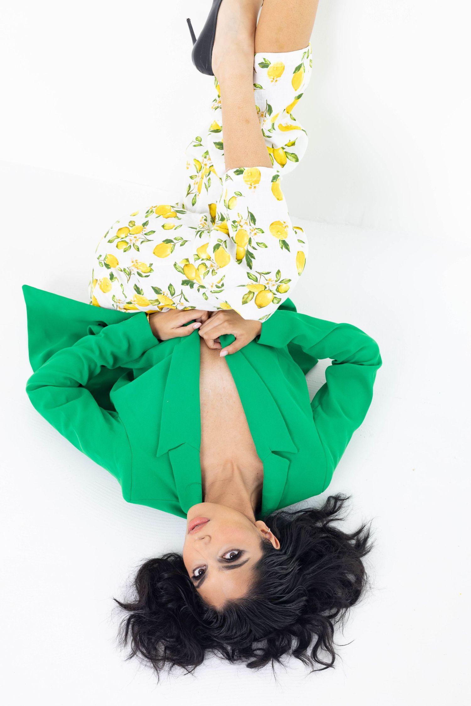 Fashion photo featuring a white dress with yellow floral print and contrasting emerald green jacket on light background.