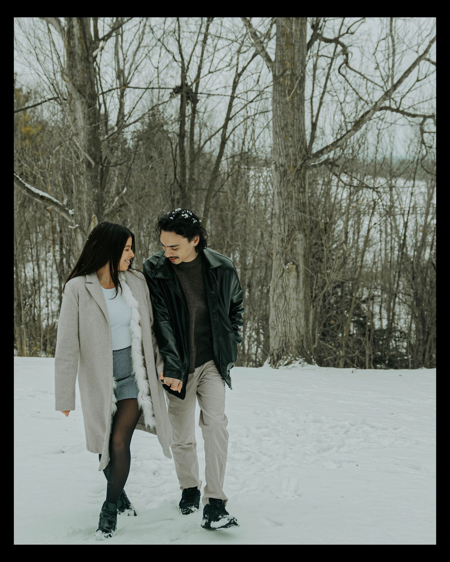 Two people walking together through a snowy winter forest scene in casual winter attire.