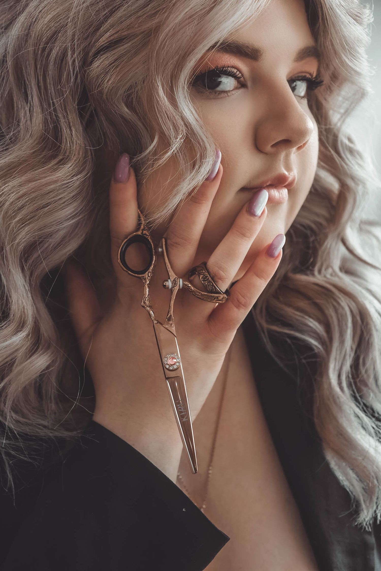 Close-up portrait showing wavy hair and jewelry with scissors pendant.
