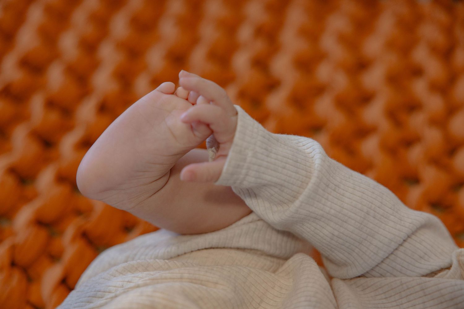 Close-up view of hands holding a white knitted or crocheted textile against an orange textured background.