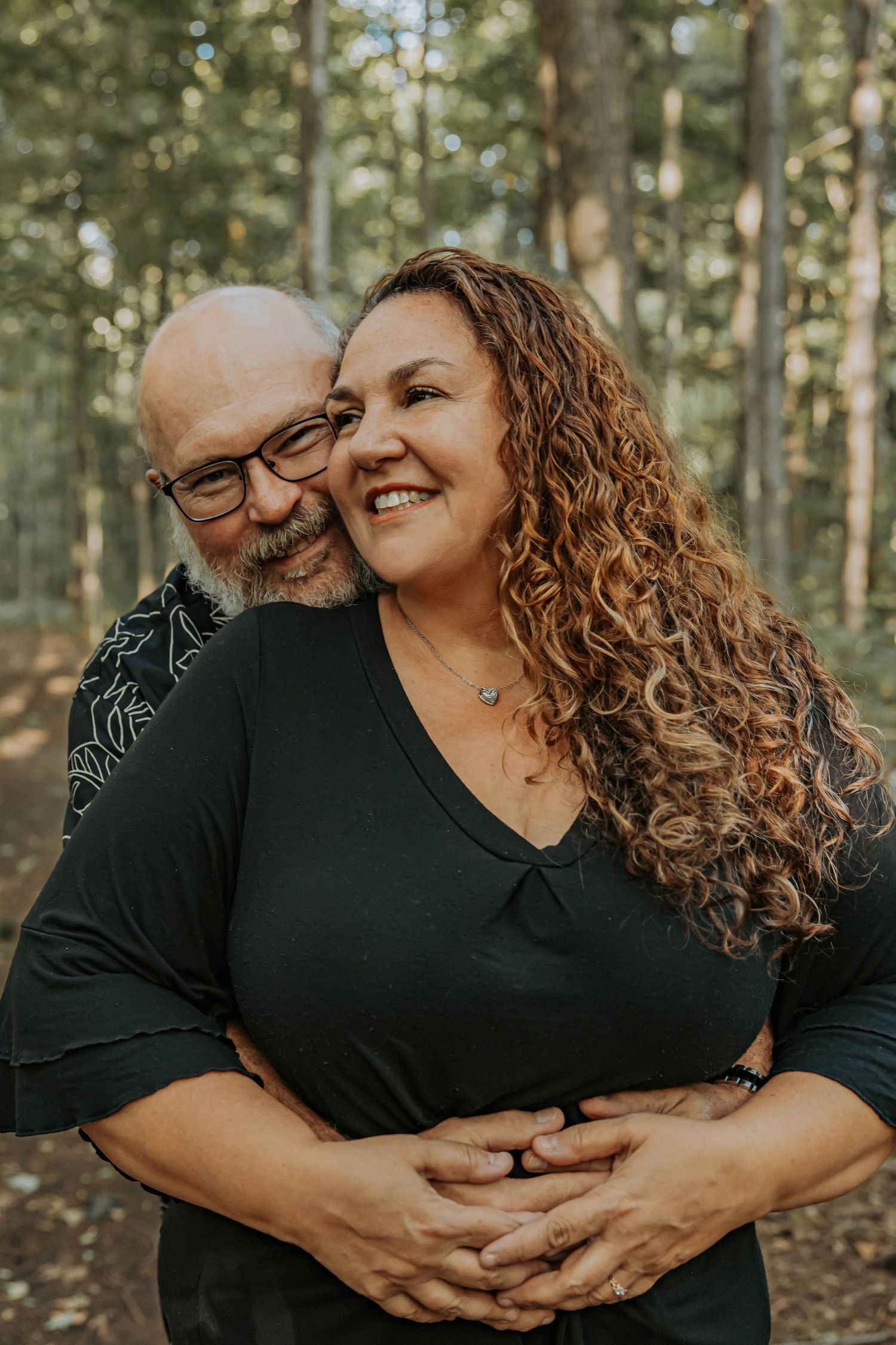 A loving couple embraces and shares joyful laughter together in a sunlit forest setting.