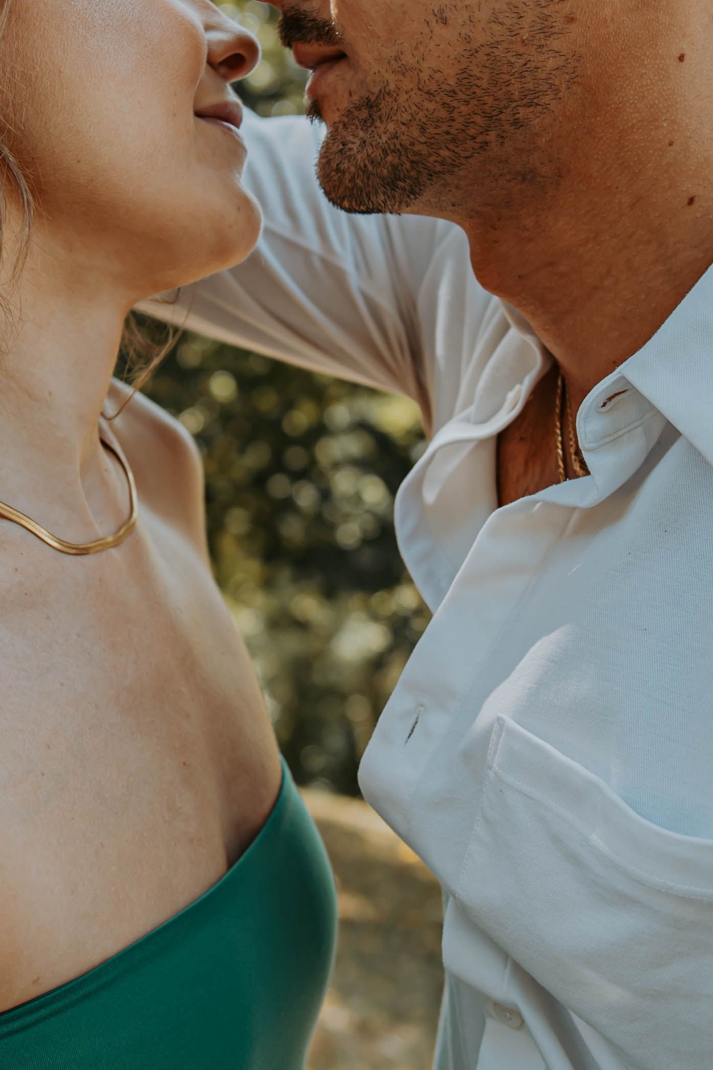 Close-up shot of a romantic couple in a tender moment outdoors, wearing a white shirt and green top against a sunlit background.